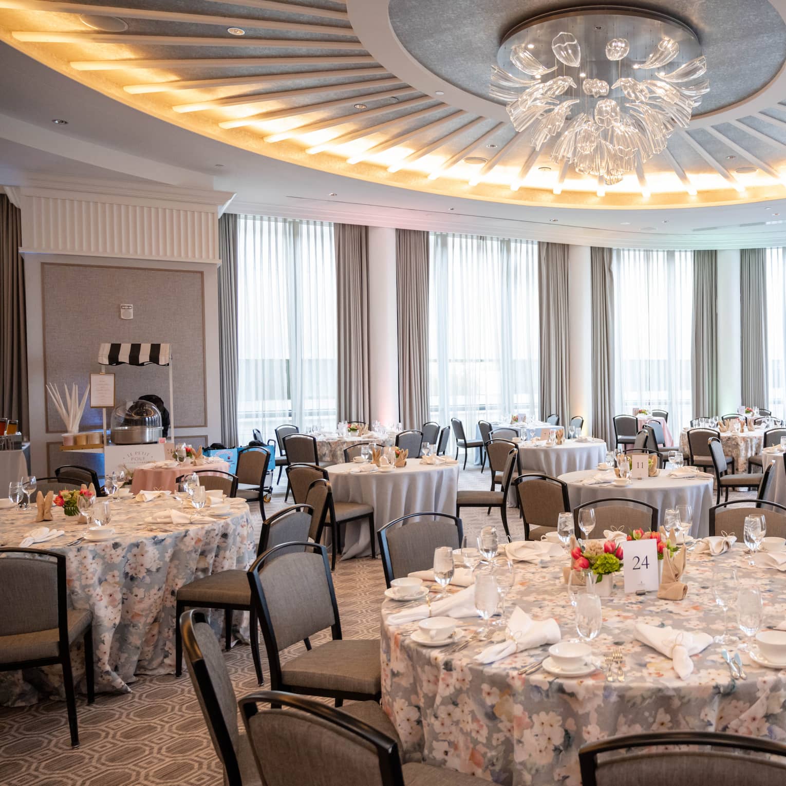 A ballroom with a chandelier and tables set with plates, napkins and glasses