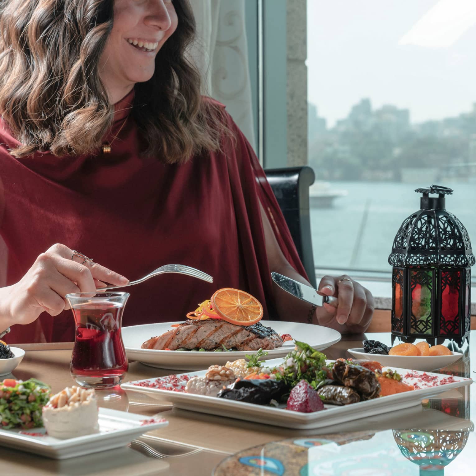 Smiling woman enjoys Ramadan feast at Zitouni, cityscape visible through window