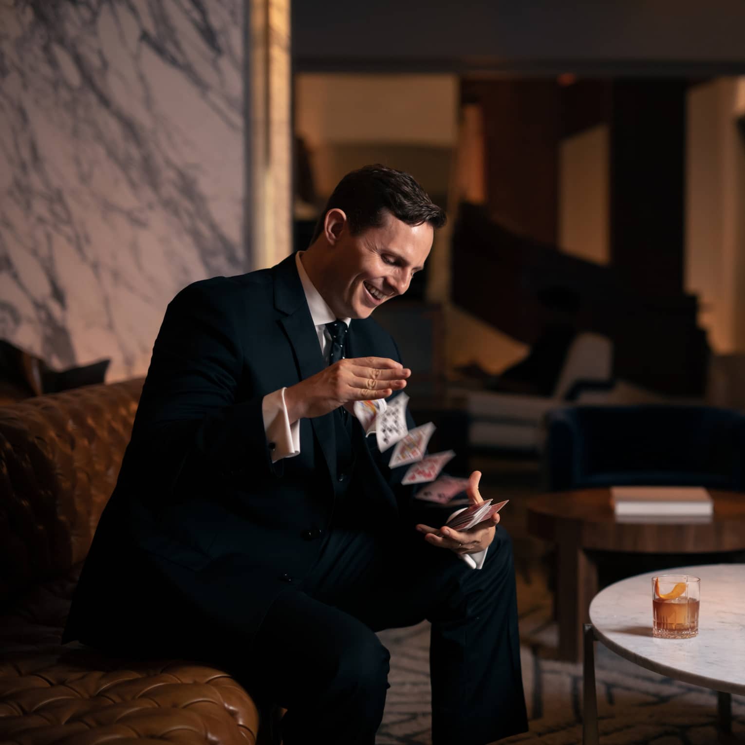 A man in a suit doing playing card drinks while sitting down.