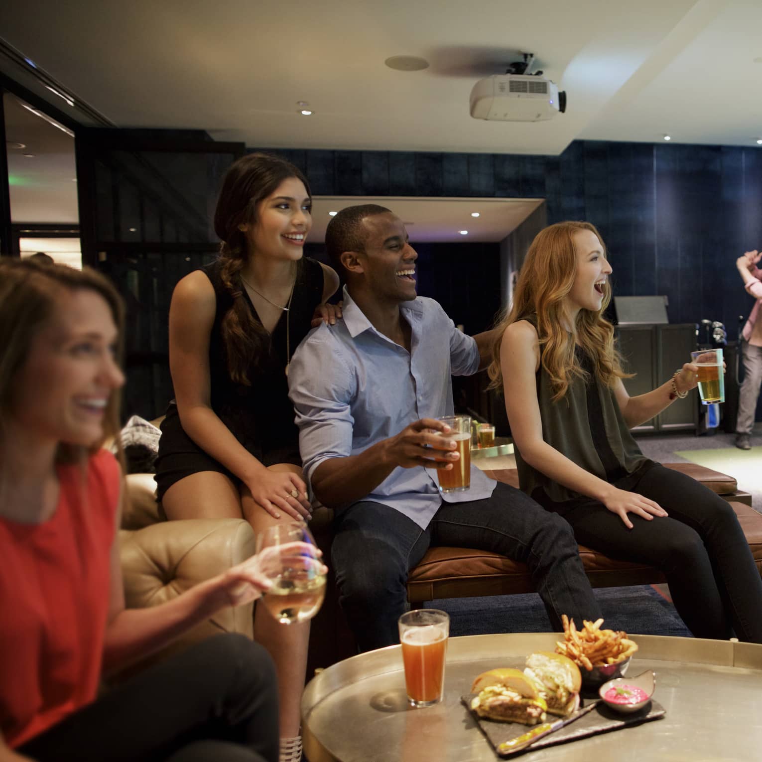 A man and three woman sip beer and cheer on a sports team in the foreground, while another man golfs in the background of a function room at four seasons hotel houston 