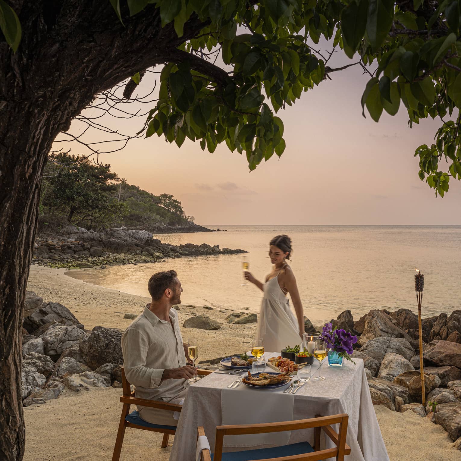 A beach dinner date at dusk, with a couple enjoying a serene seaside view.