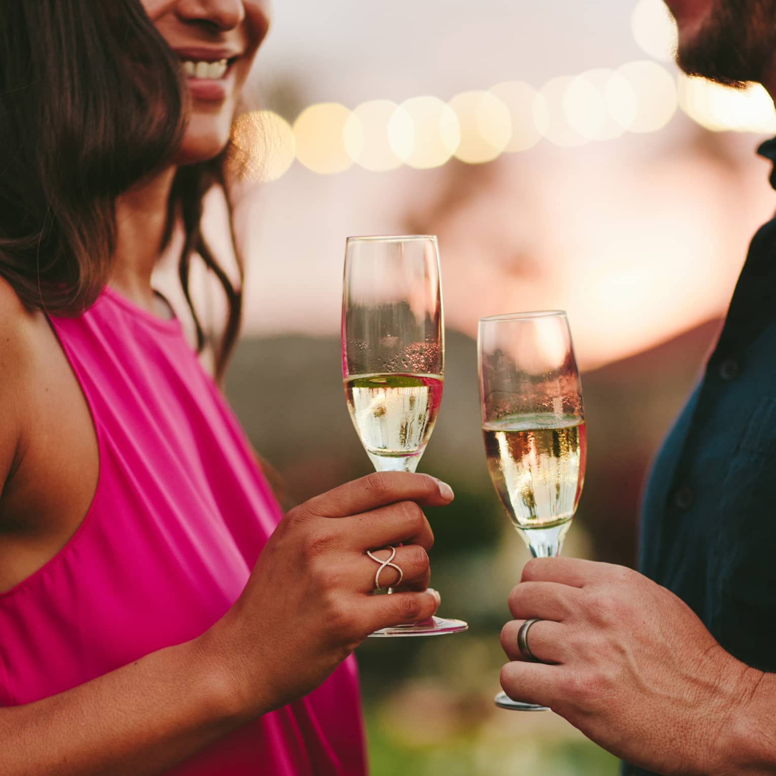 A woman in a fuscia pink dress hold a glass of champagne next to a man with a navy shirt holding his own glass