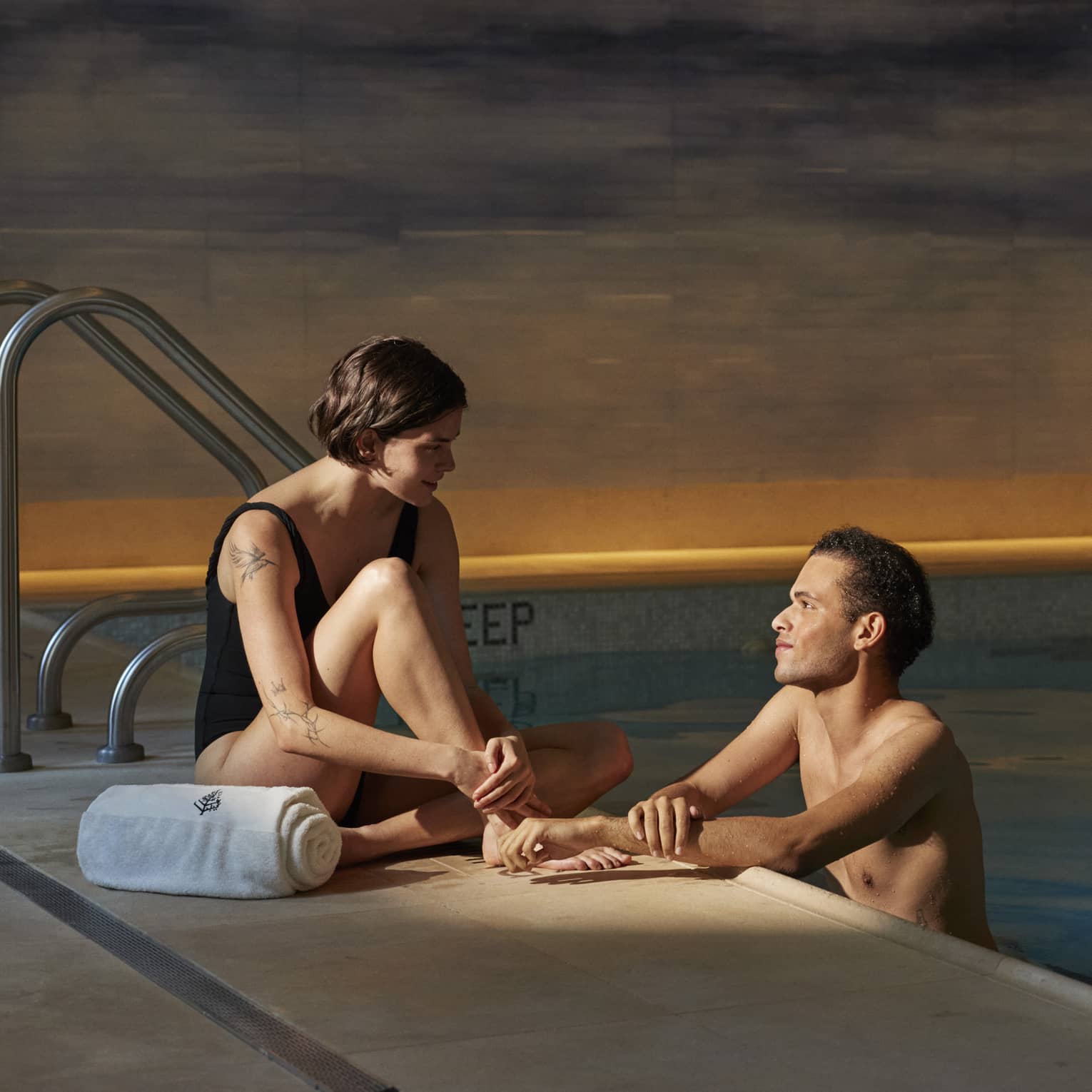 Person sitting poolside with a towel talking to another person leaning on the edge of the pool at Four Seasons luxury hotel