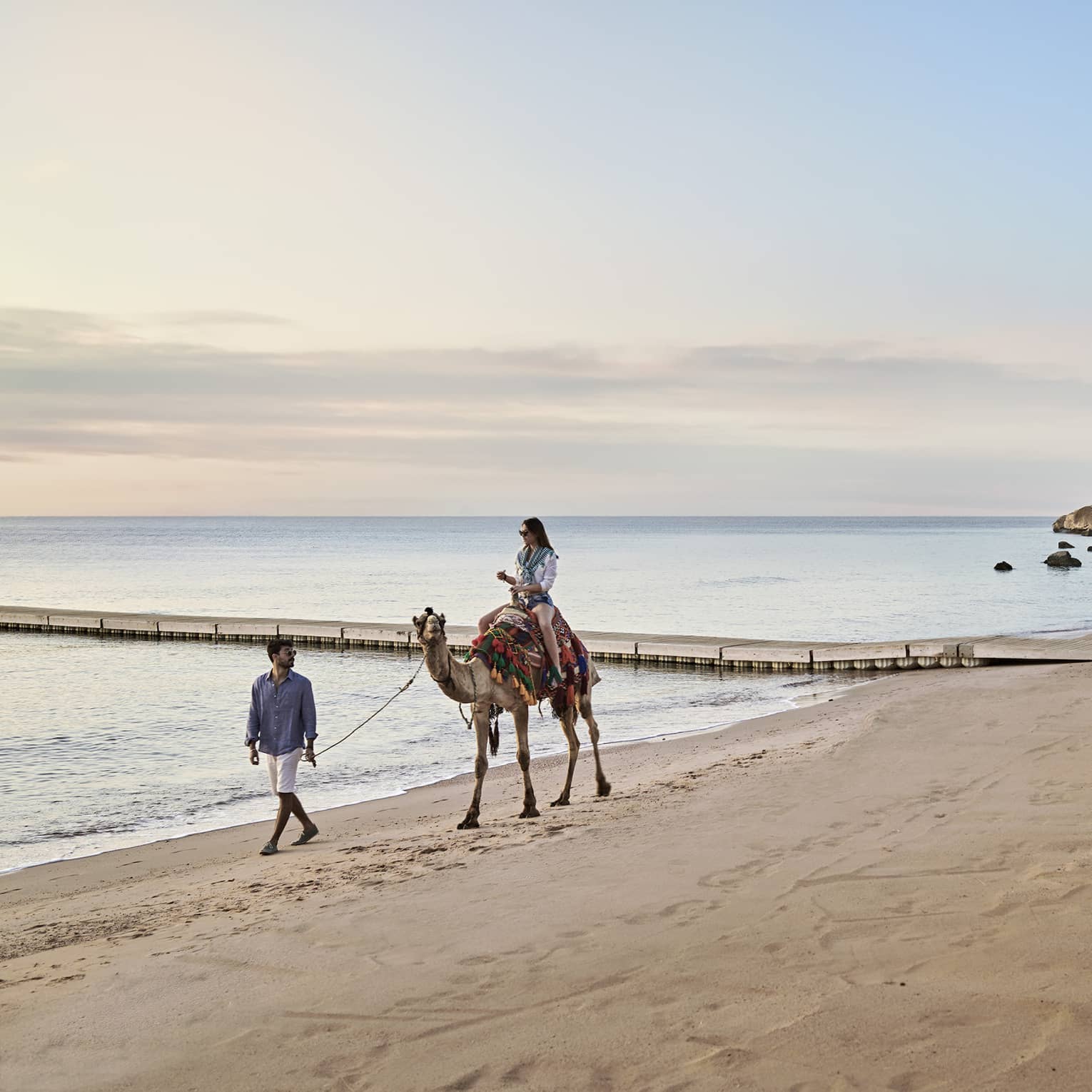 A woman rides a camel, led by a man, along the beach at Four Seasons Sharm El Sheikh