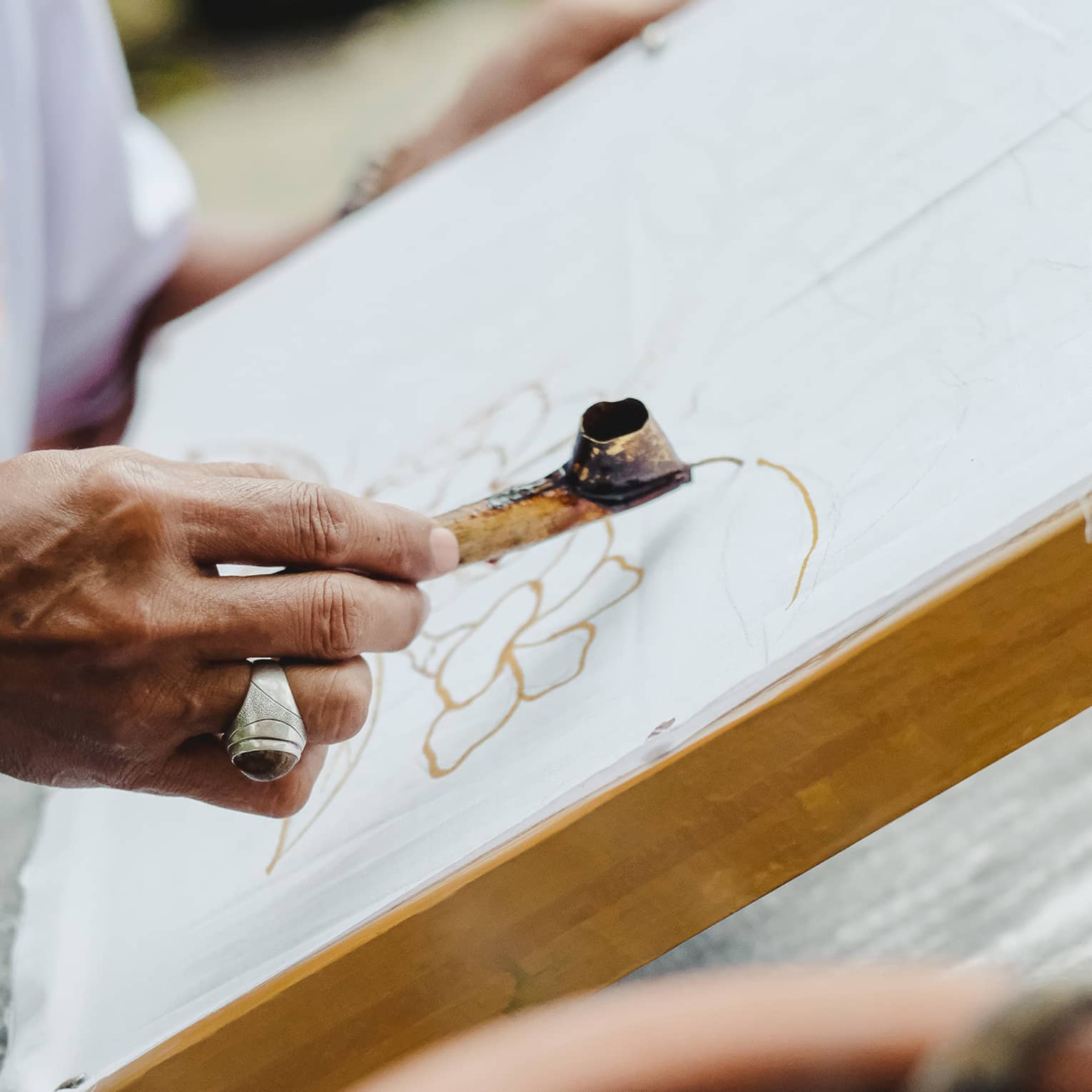 Close-up of someone using a metal Canting pen to draw a pattern in wax on a flat canvas.