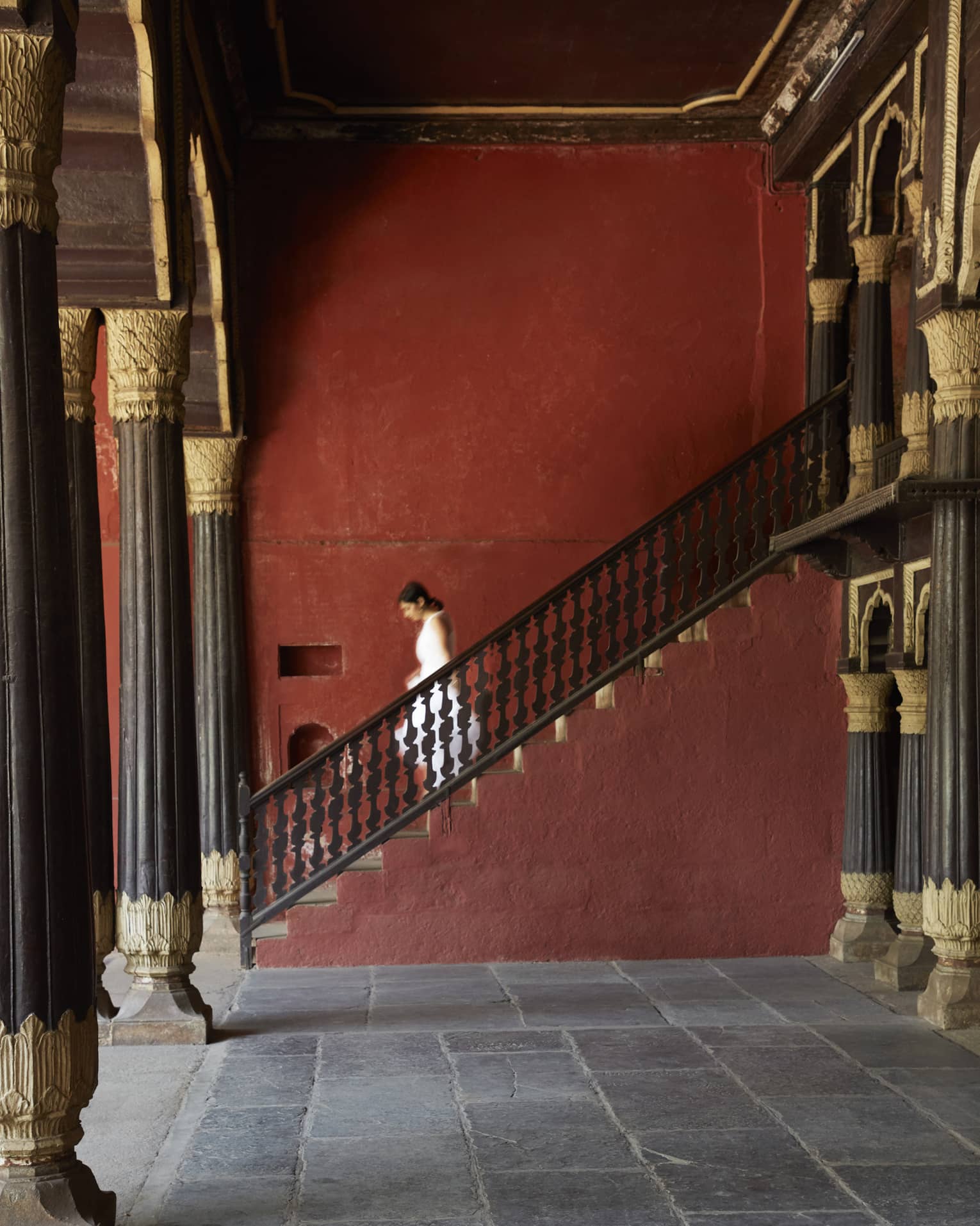 Side view of a guest descending a stone staircase, in a room supported by pillars with intricate gilded embellishments.