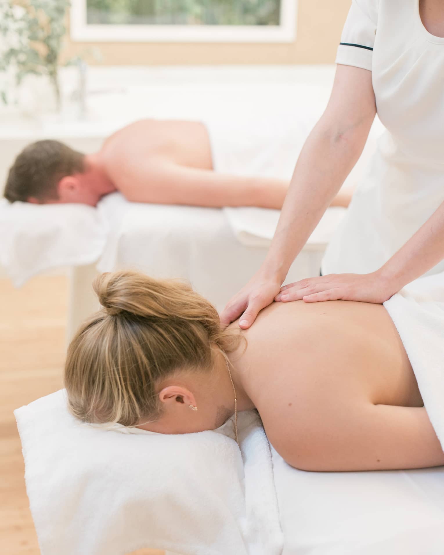 Two people laying on massage tables with blankets while getting a massage.