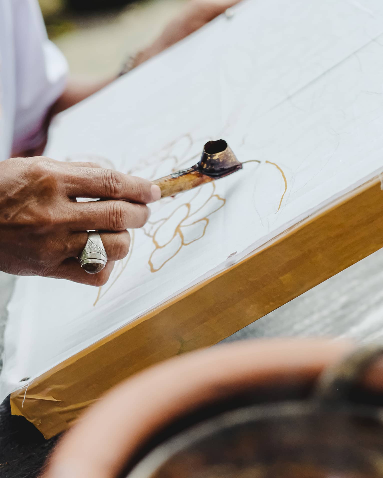 Close-up of someone using a metal Canting pen to draw a pattern in wax on a flat canvas. 