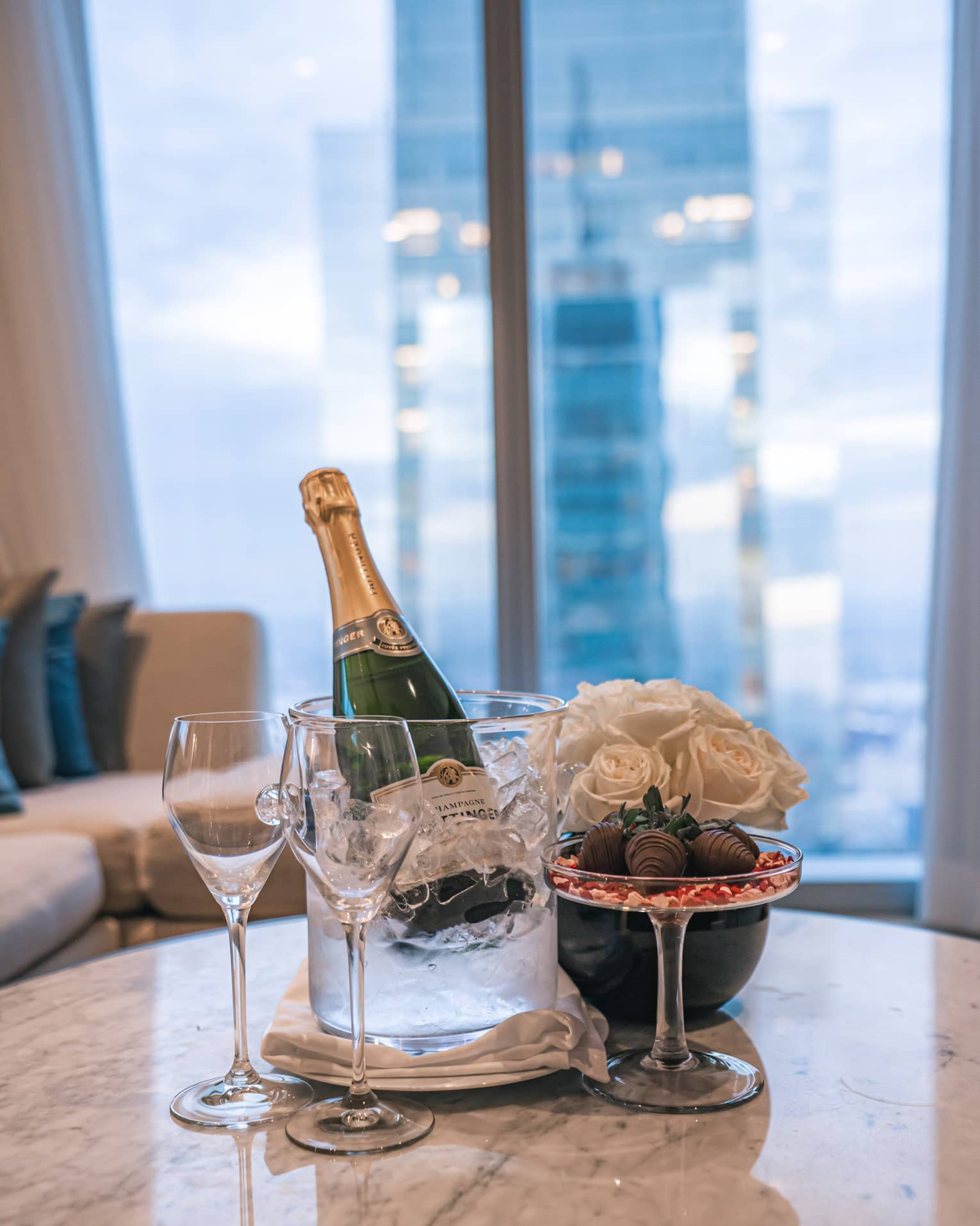 A bottle of Champagne next to a vase of flowers and glasses.