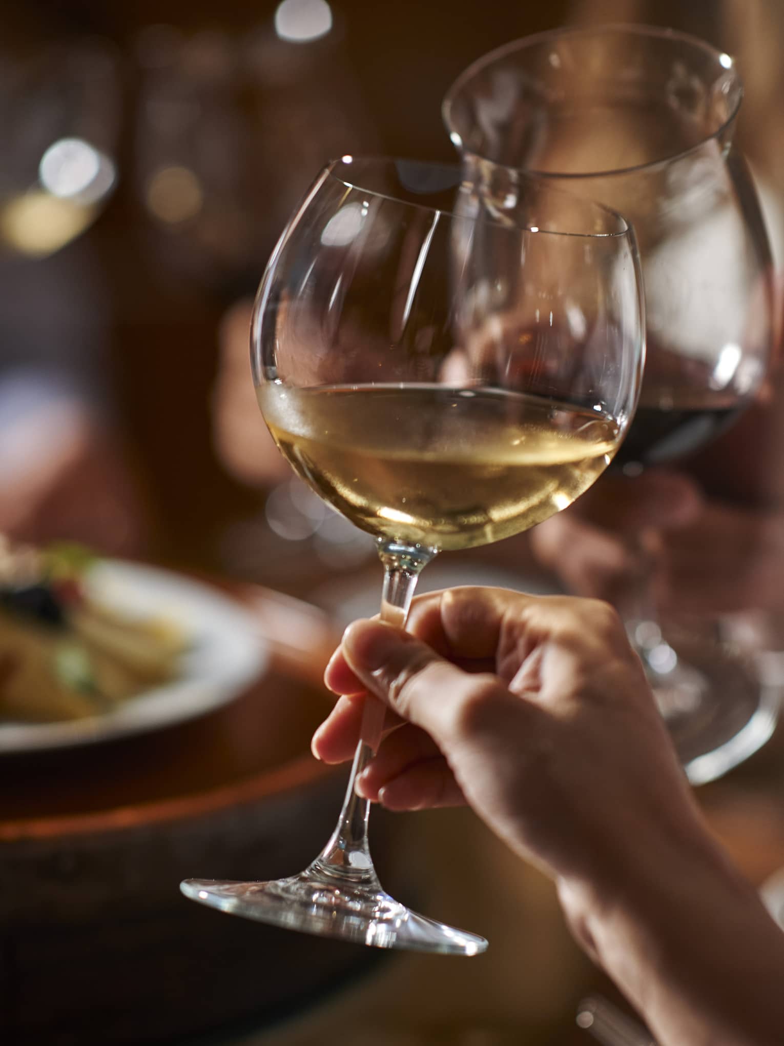 Two guests clink their wine glasses together at dinner