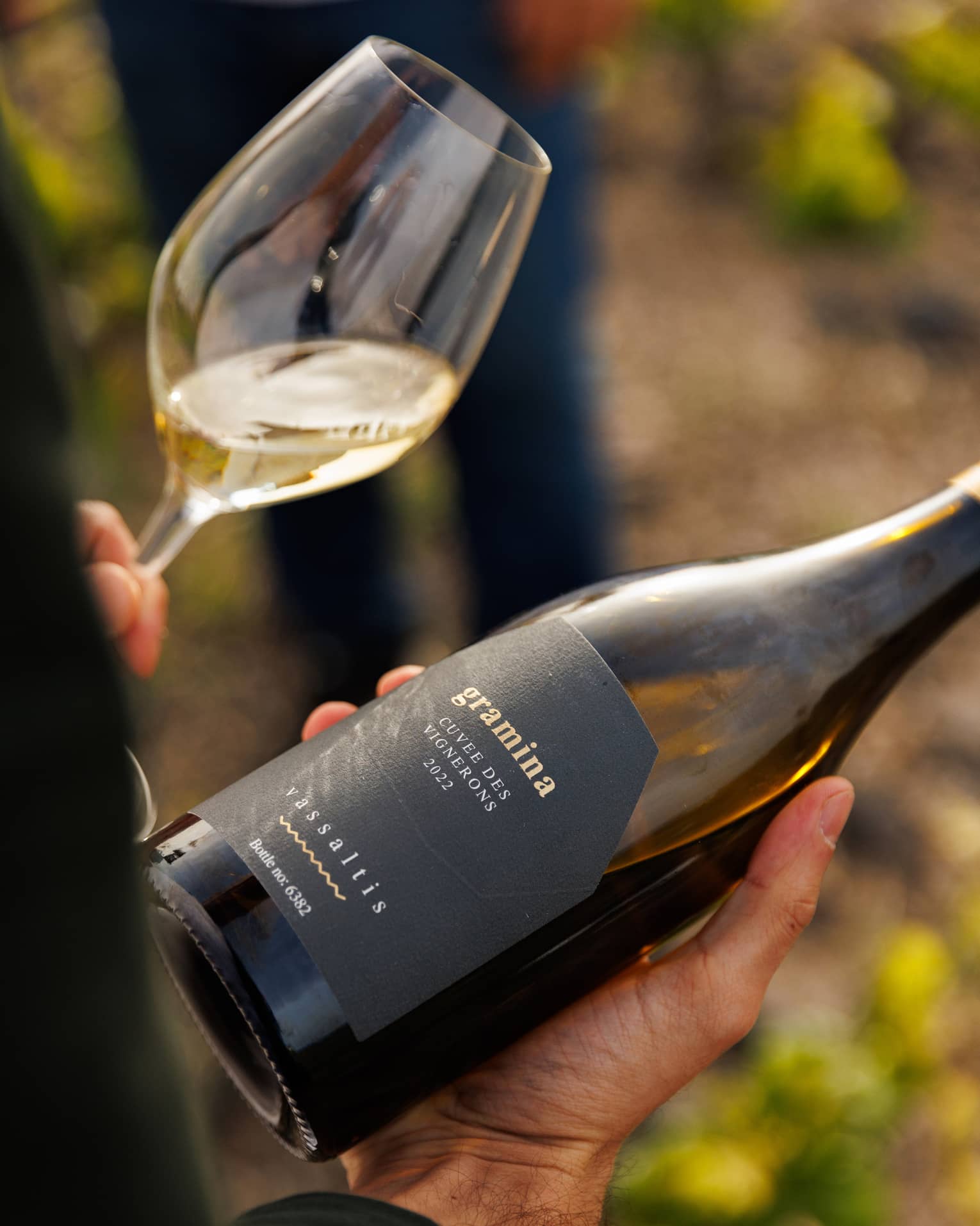 Person holding wine bottle in right hand and glass of white wine in left hand