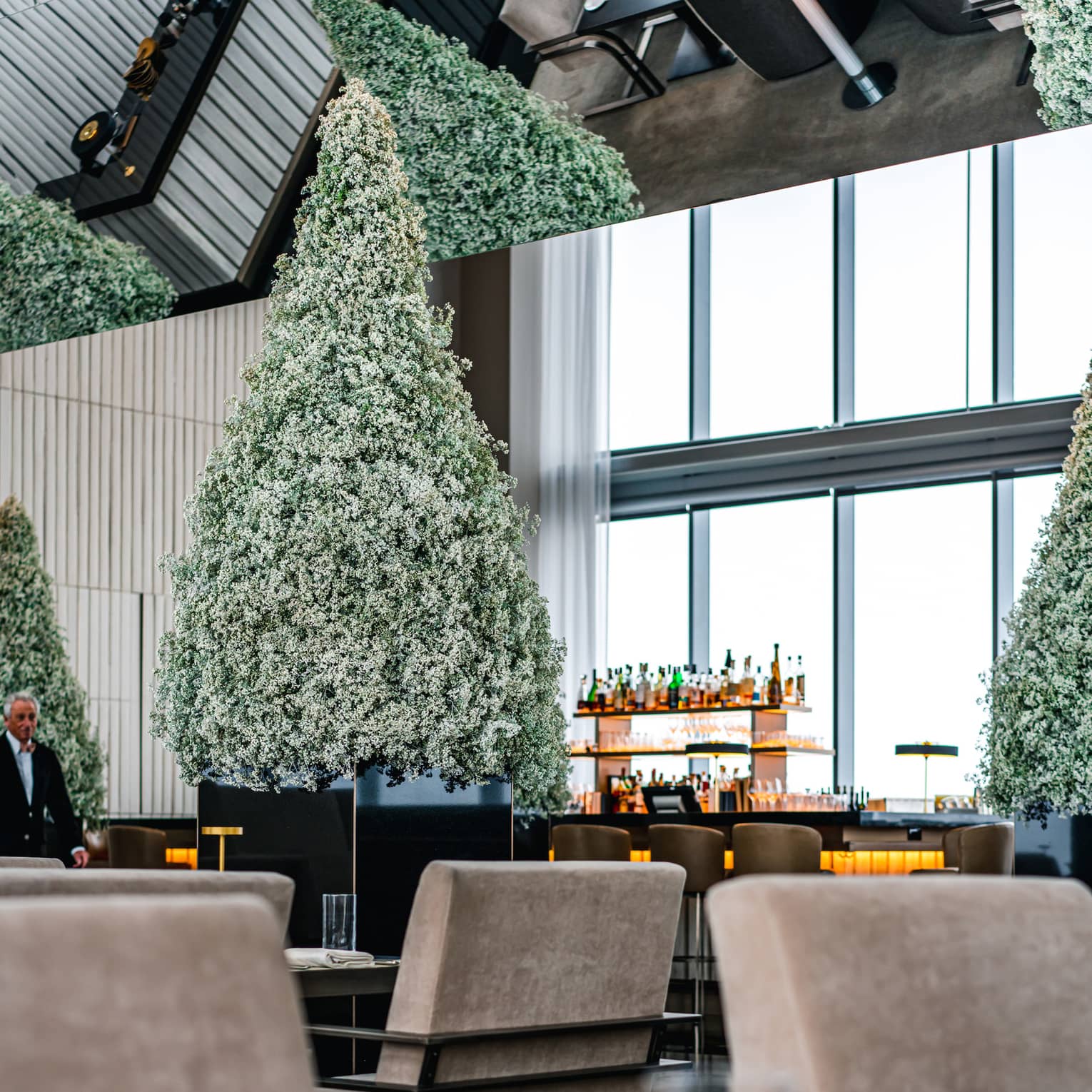 A dining area with beige chairs and place mats, Christmas trees and a bar can be seen on the other side of the room.