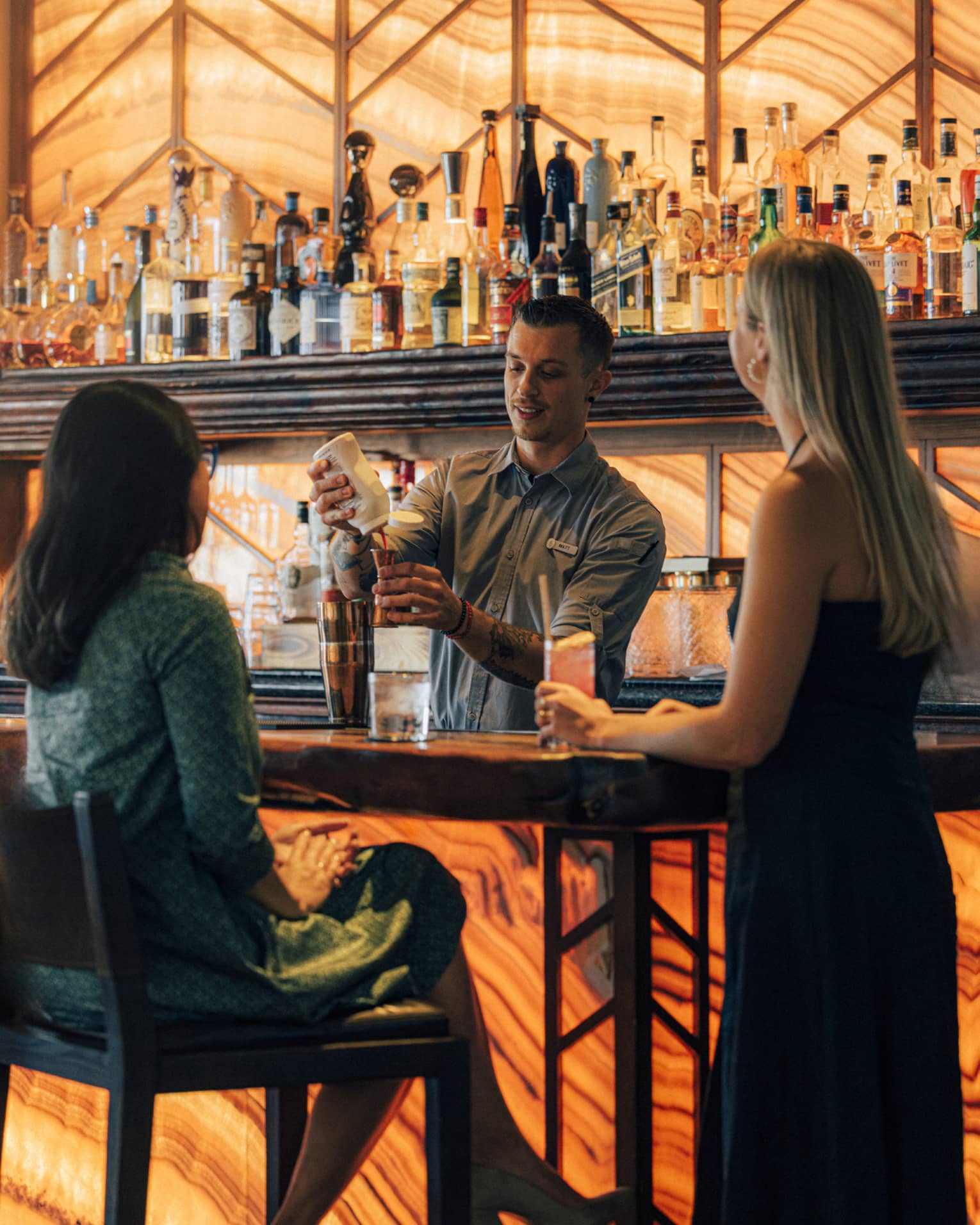 Two guests at the bar while the bartender is making a drink.