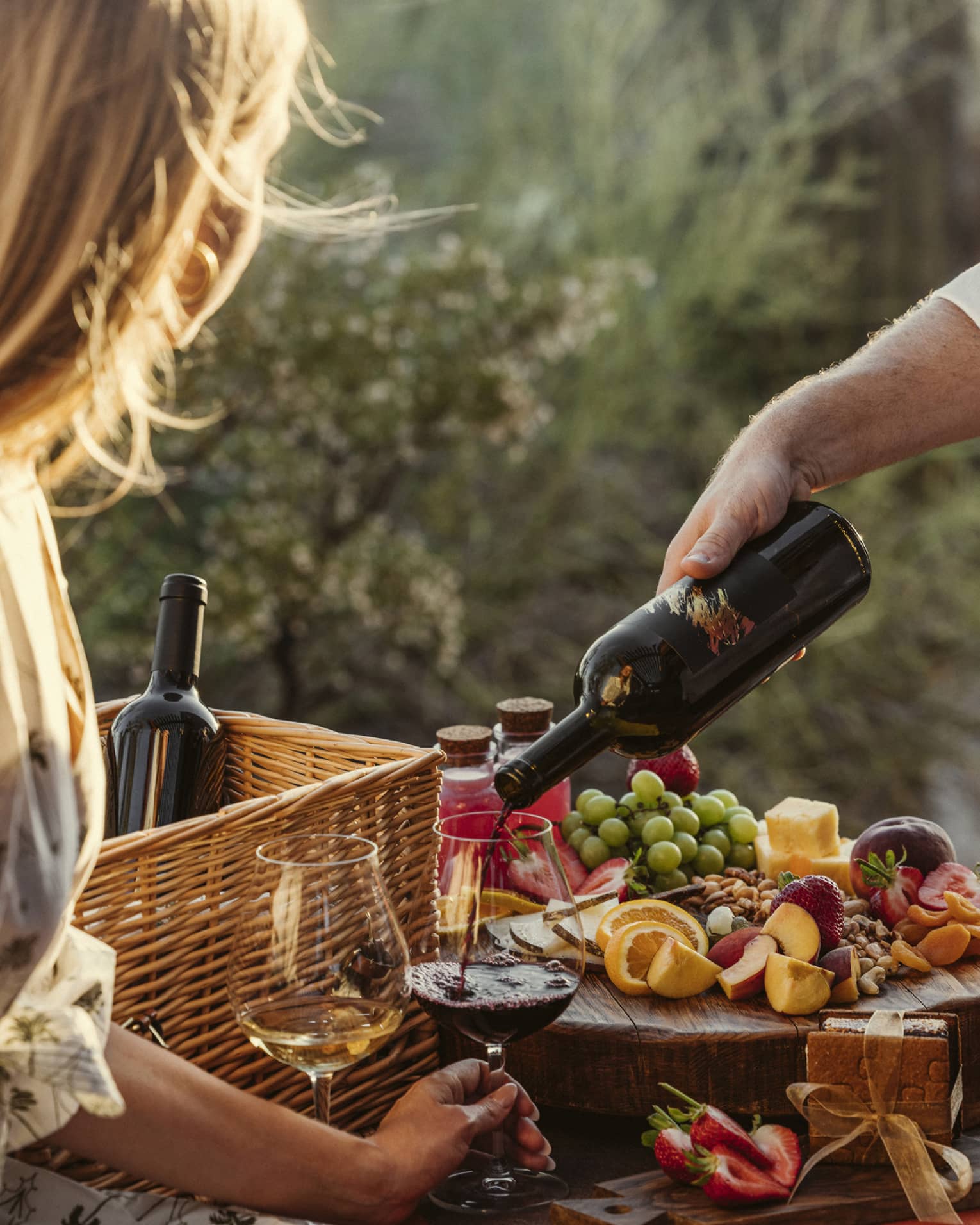 Guest eating a picnic outside with wine glasses and a fruit spread.