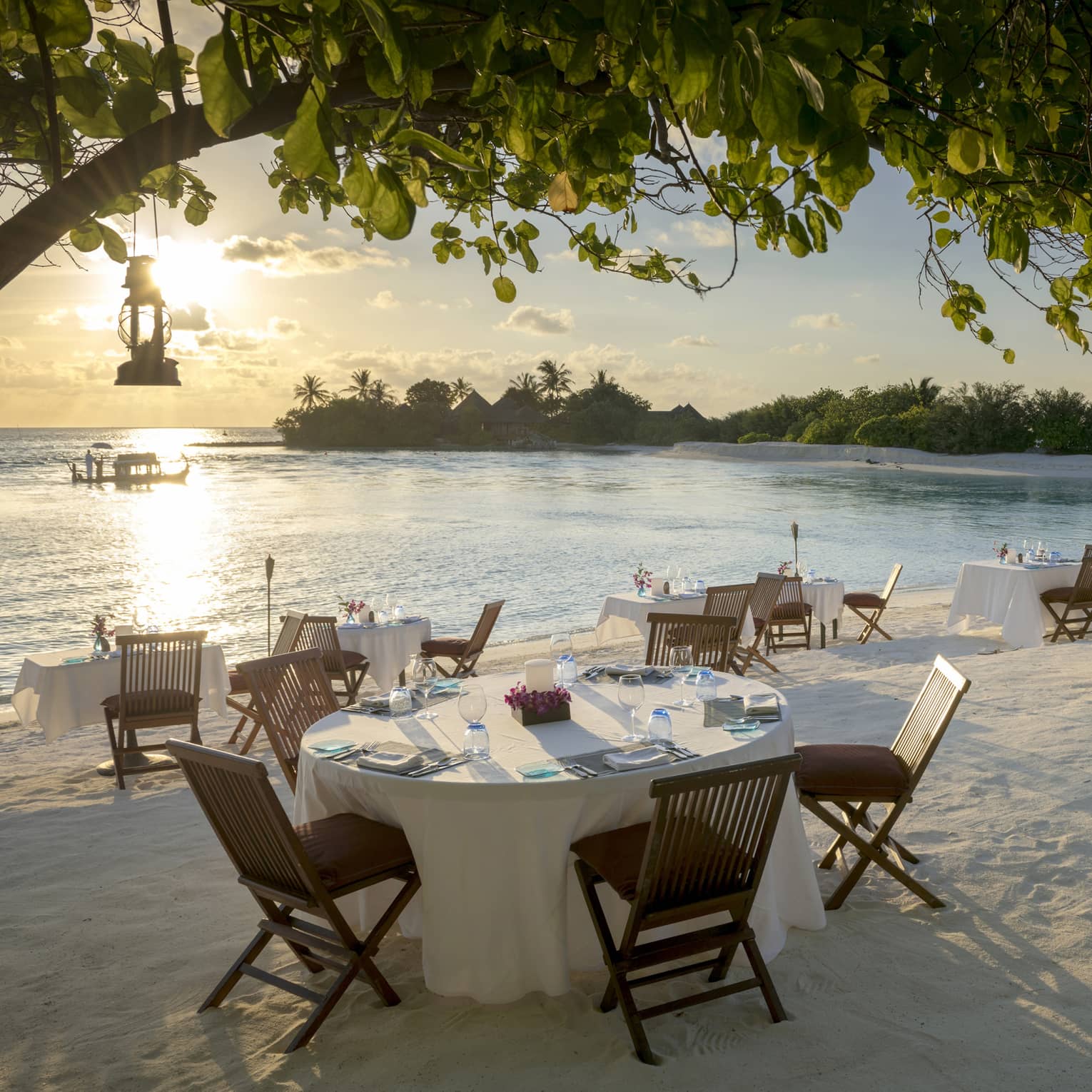 Tables set for dinner with wooden chairs on white sand by ocean shore