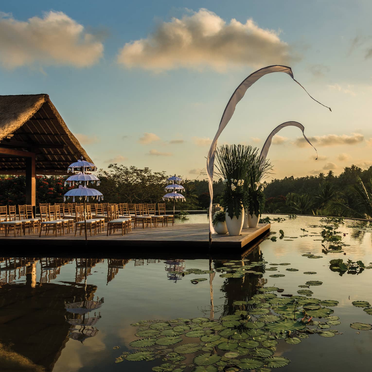 Rows of chairs set up for wedding ceremony on patio over lotus pond at sunset