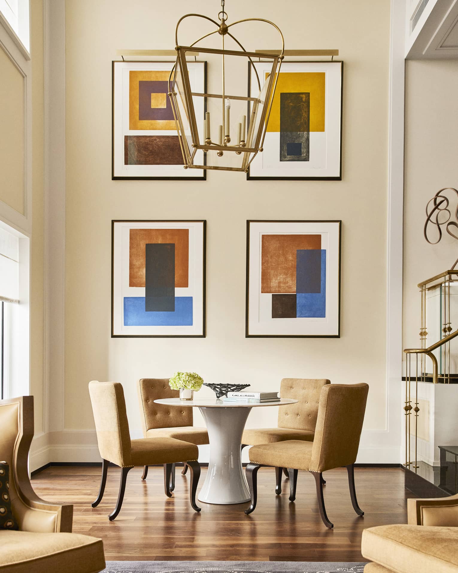 Round table with four brown upholstered chairs beside tall wall with four abstract art pieces
