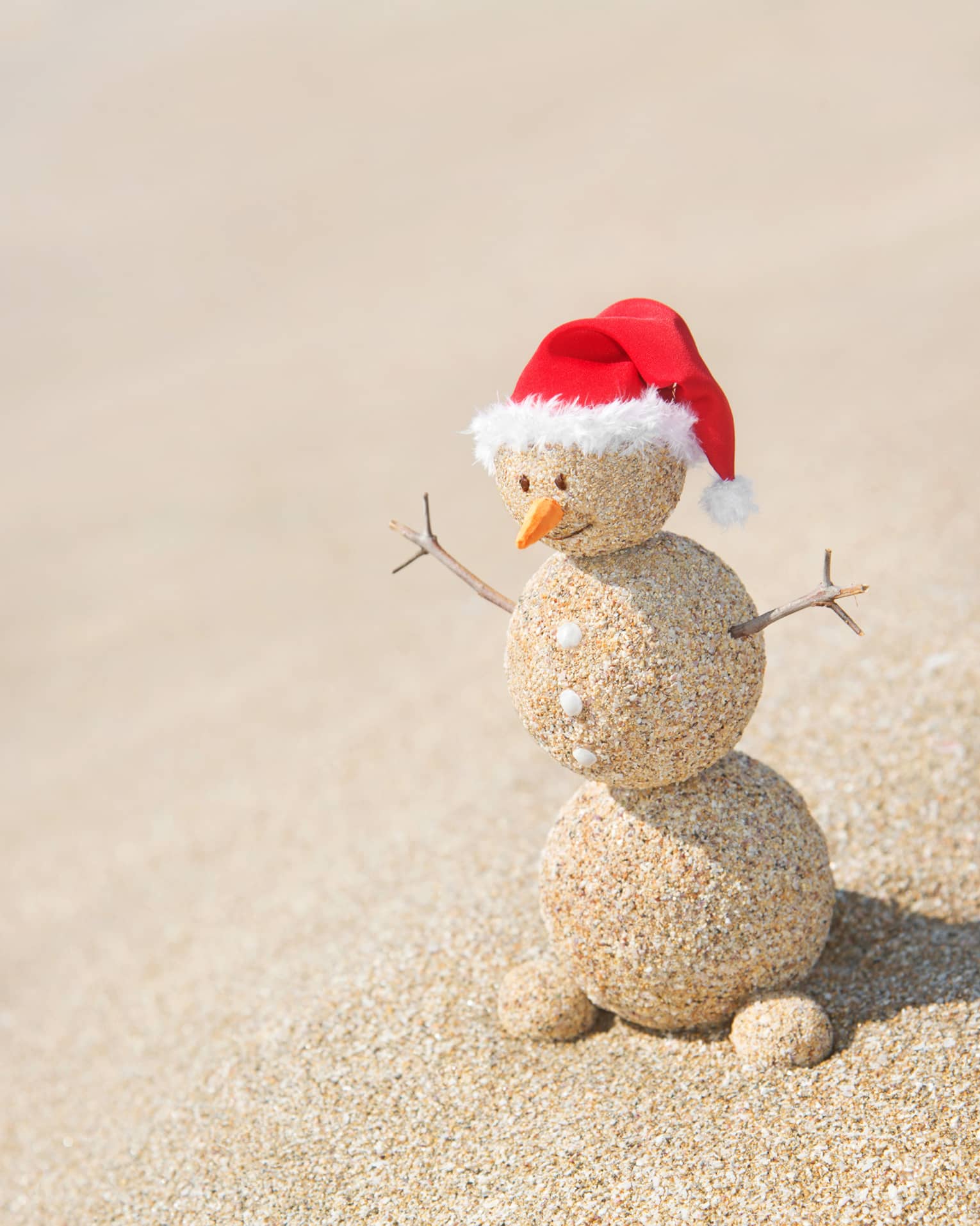 A snowman made out of sand with a red Santa hat.