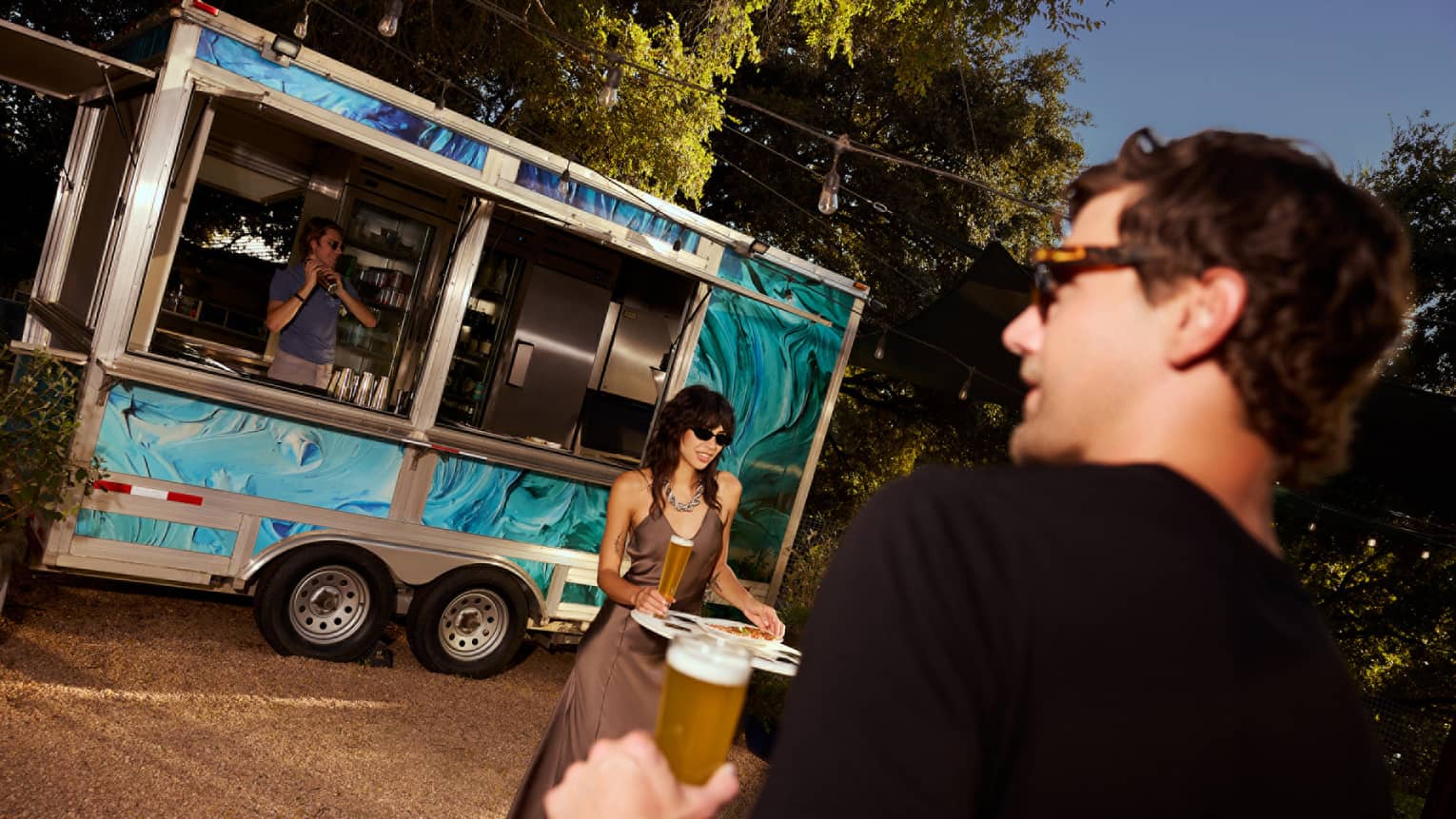 A couple dressed in formal attire holding tall glasses of beer in front of a blue food truck