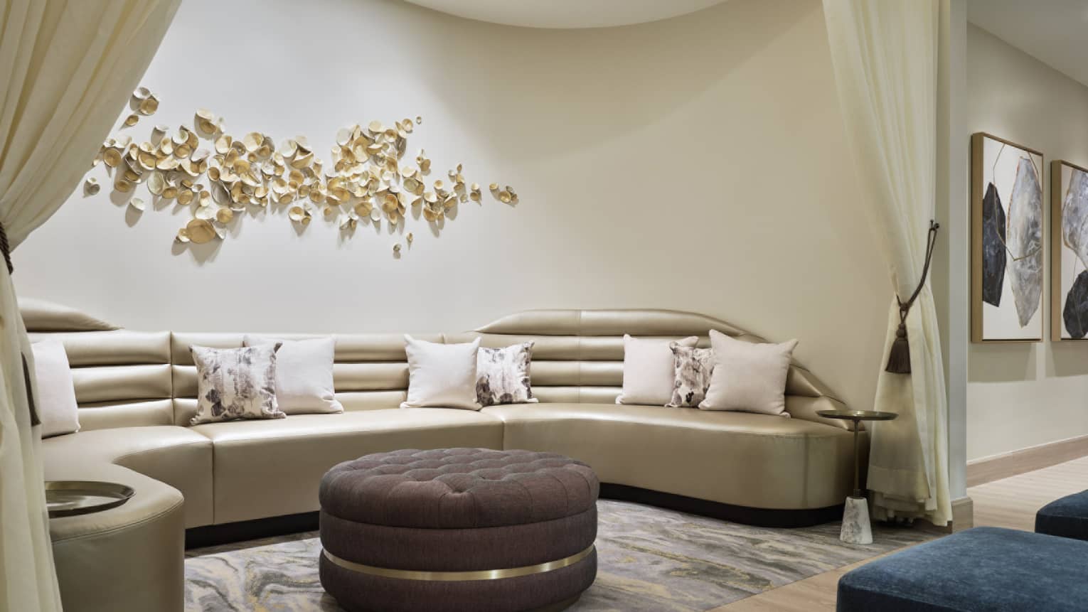 Gold L shaped couch with ottoman and curtains.