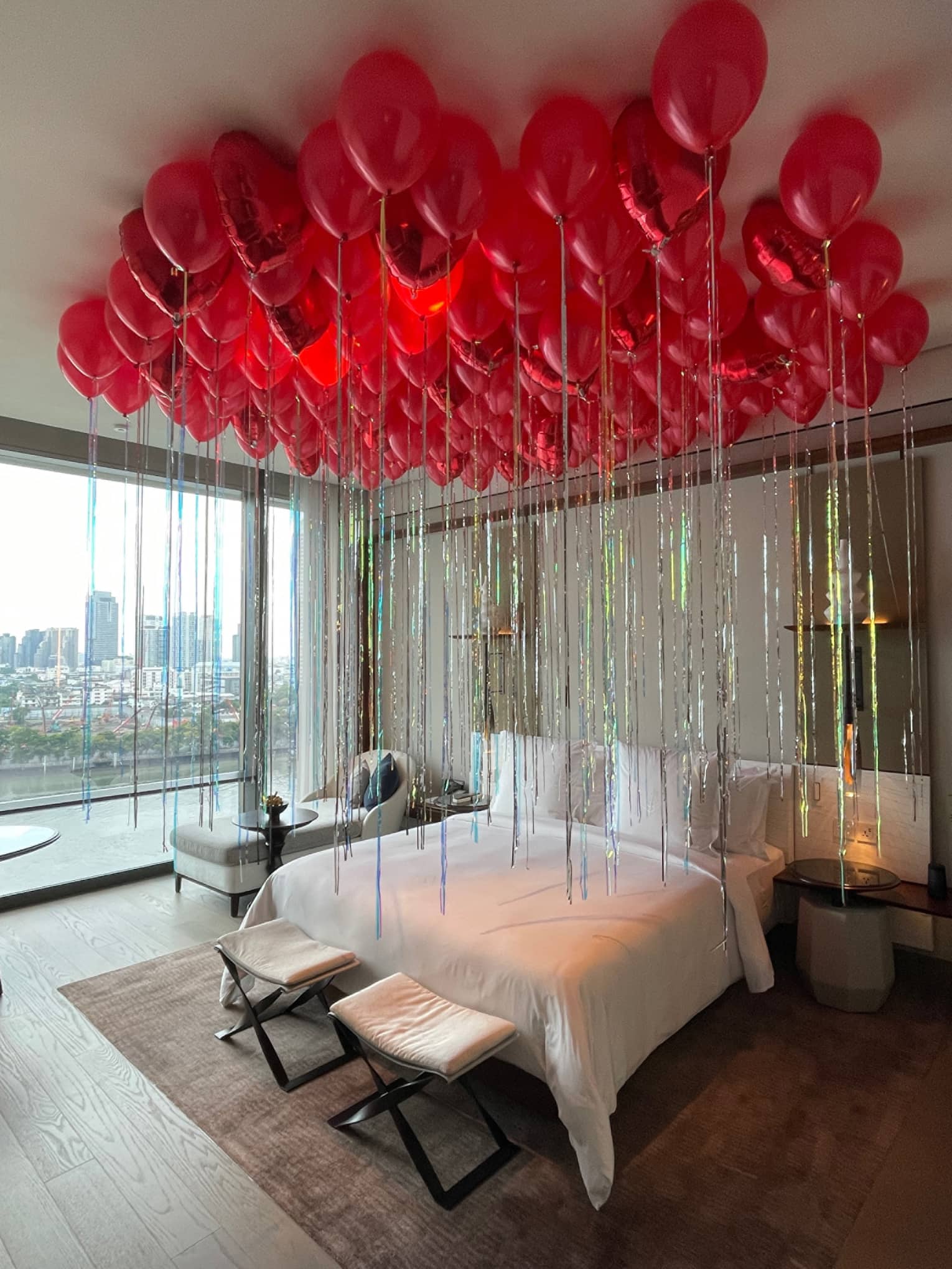 Dozens of shiny red balloons with strings hover on ceiling over hotel bed