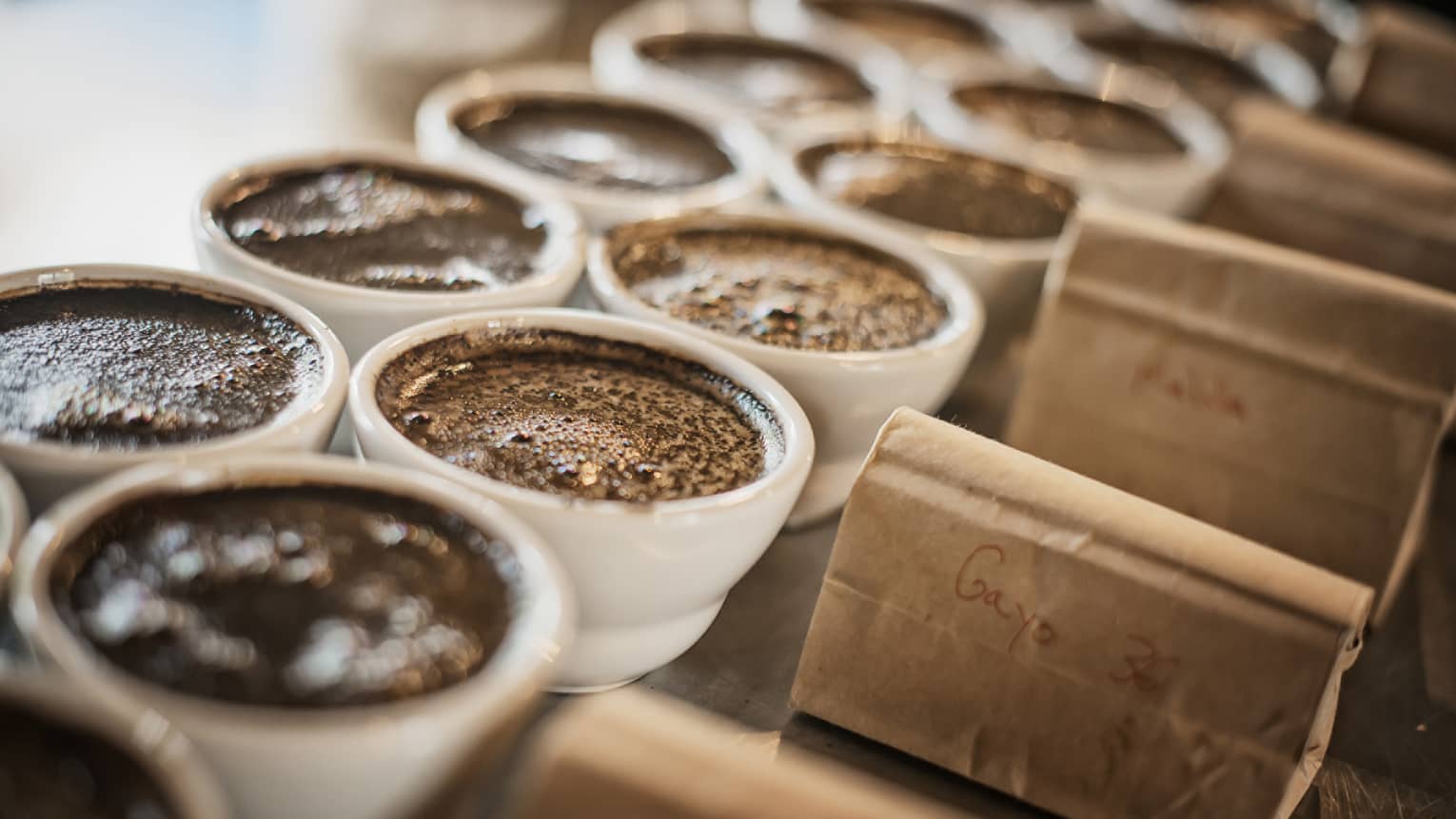 Dark coffee in white porcelain ramekins next to kraft paper bags.