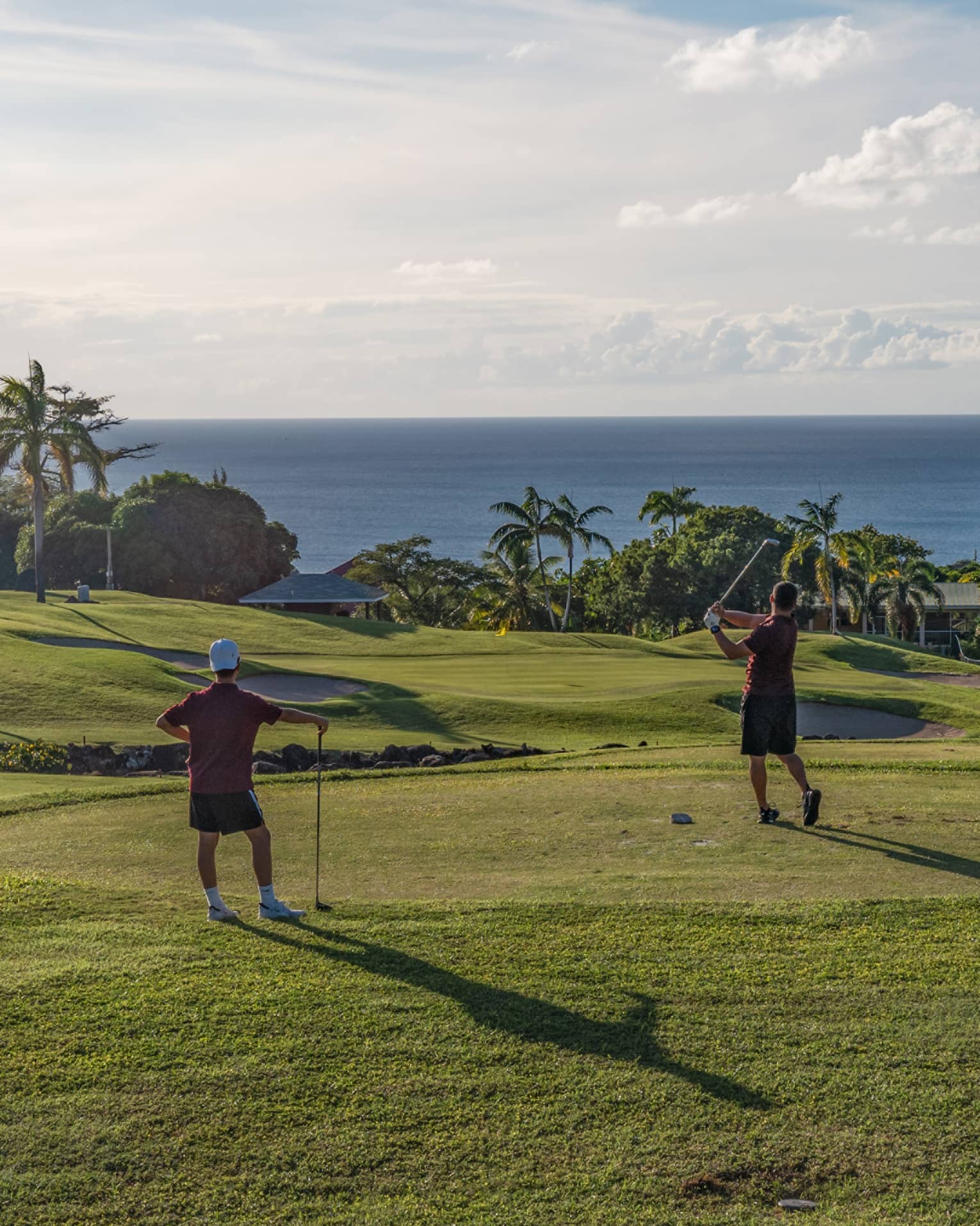 Two guests on a golf course near the ocean swinging golf clubs