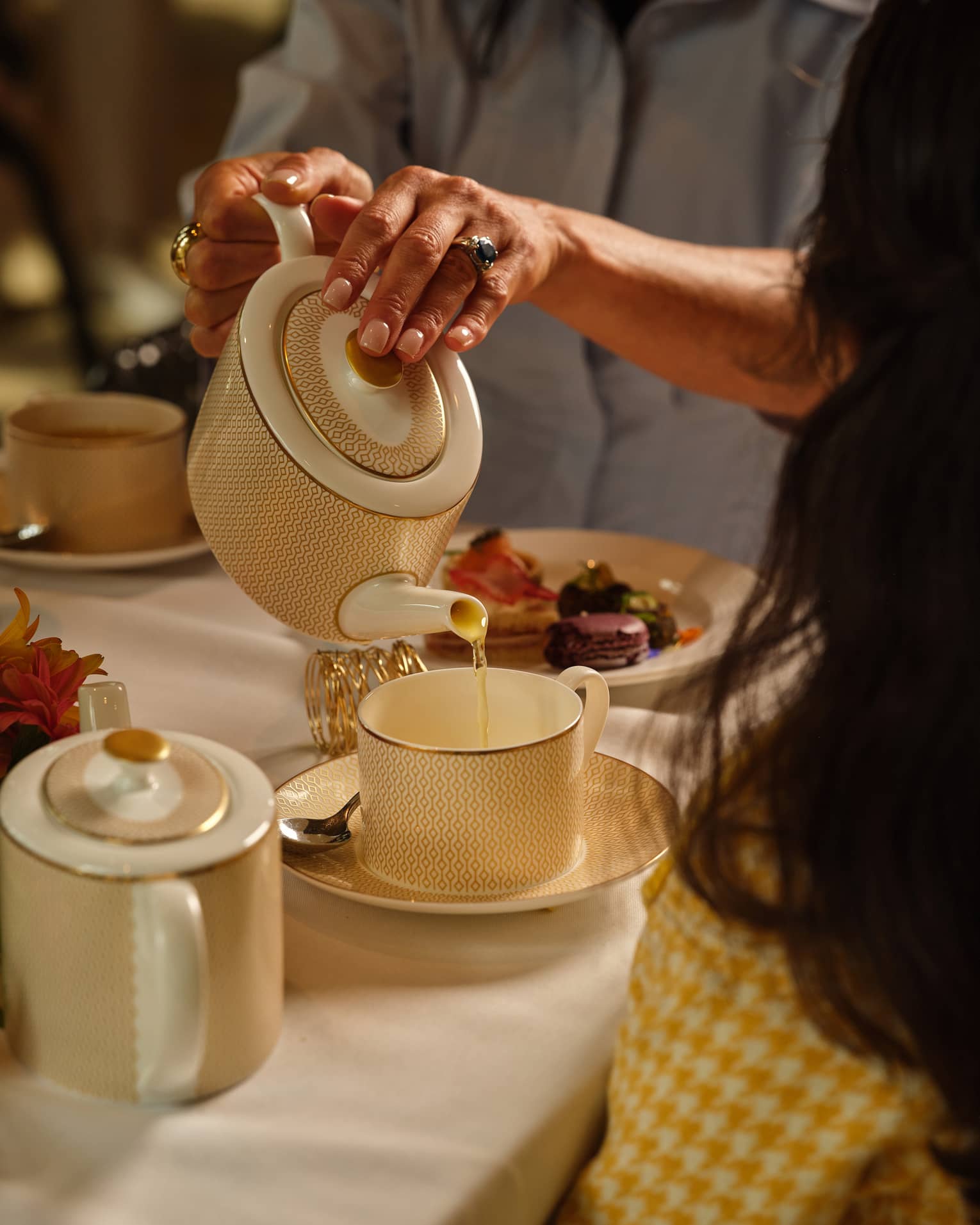Person pours tea from a cream porcelain tea pot into a matching mug