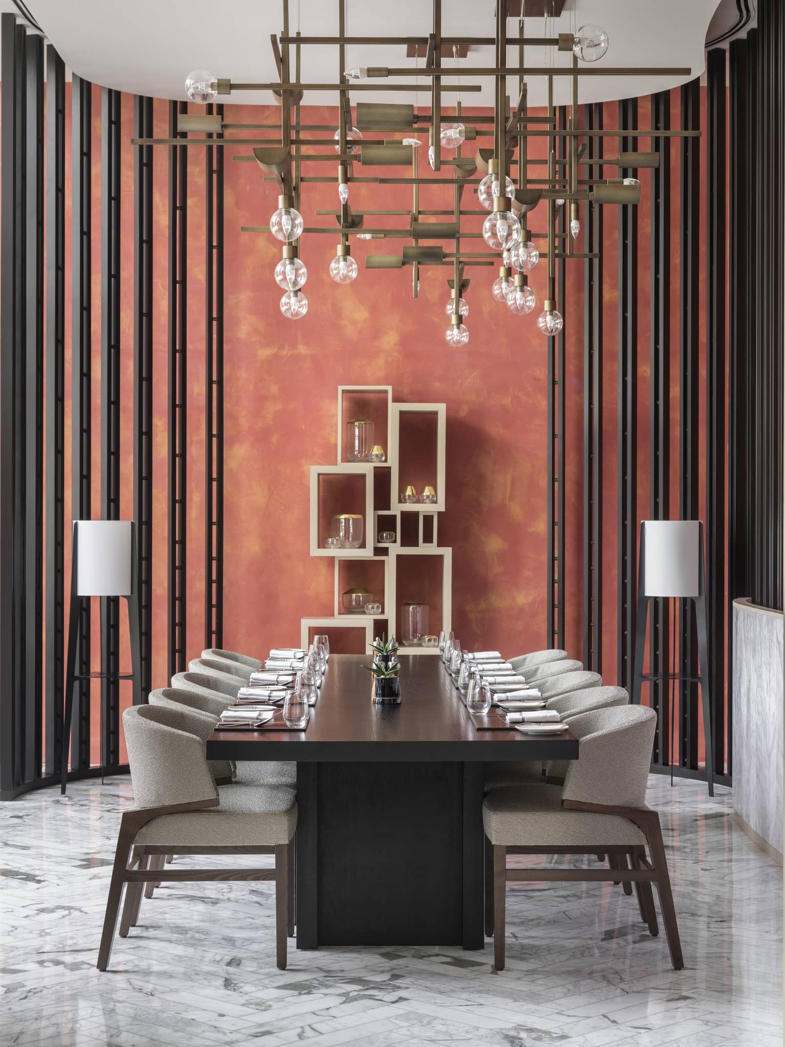 A sculptural lighting fixture hangs above a set table in a coral dining room