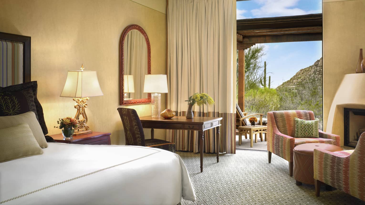 Premier Casita Room corner of bed, desk, armchairs by gas fireplace, mountain views through open balcony door