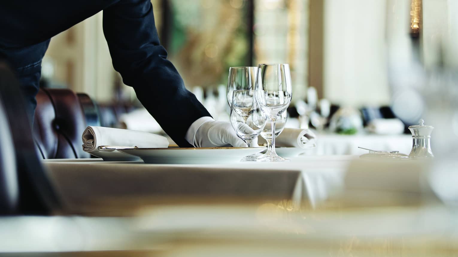 A white-gloved hand arranges a place-setting on a clothed table