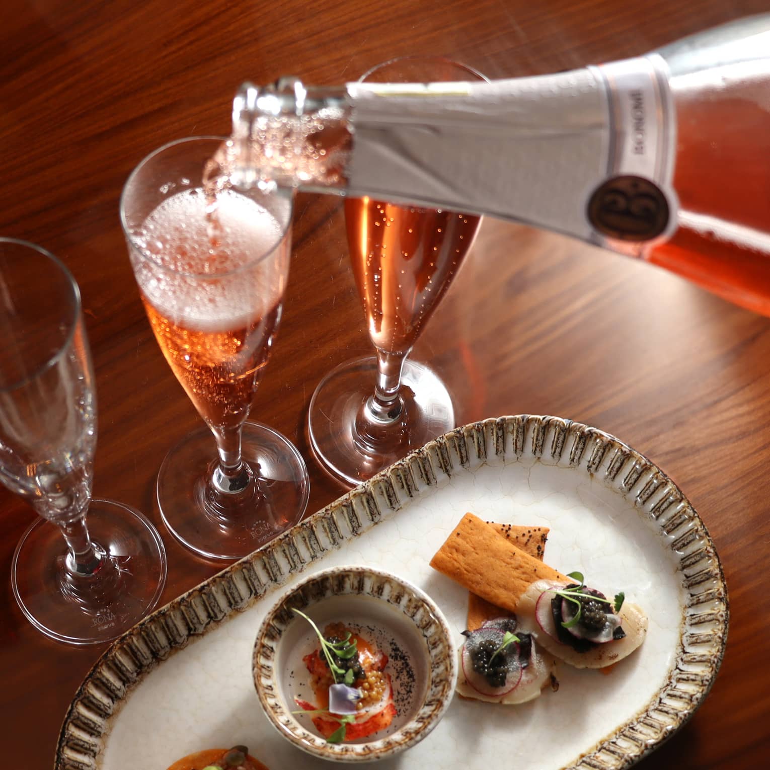 Champagne being poured into a glass beside a food dish