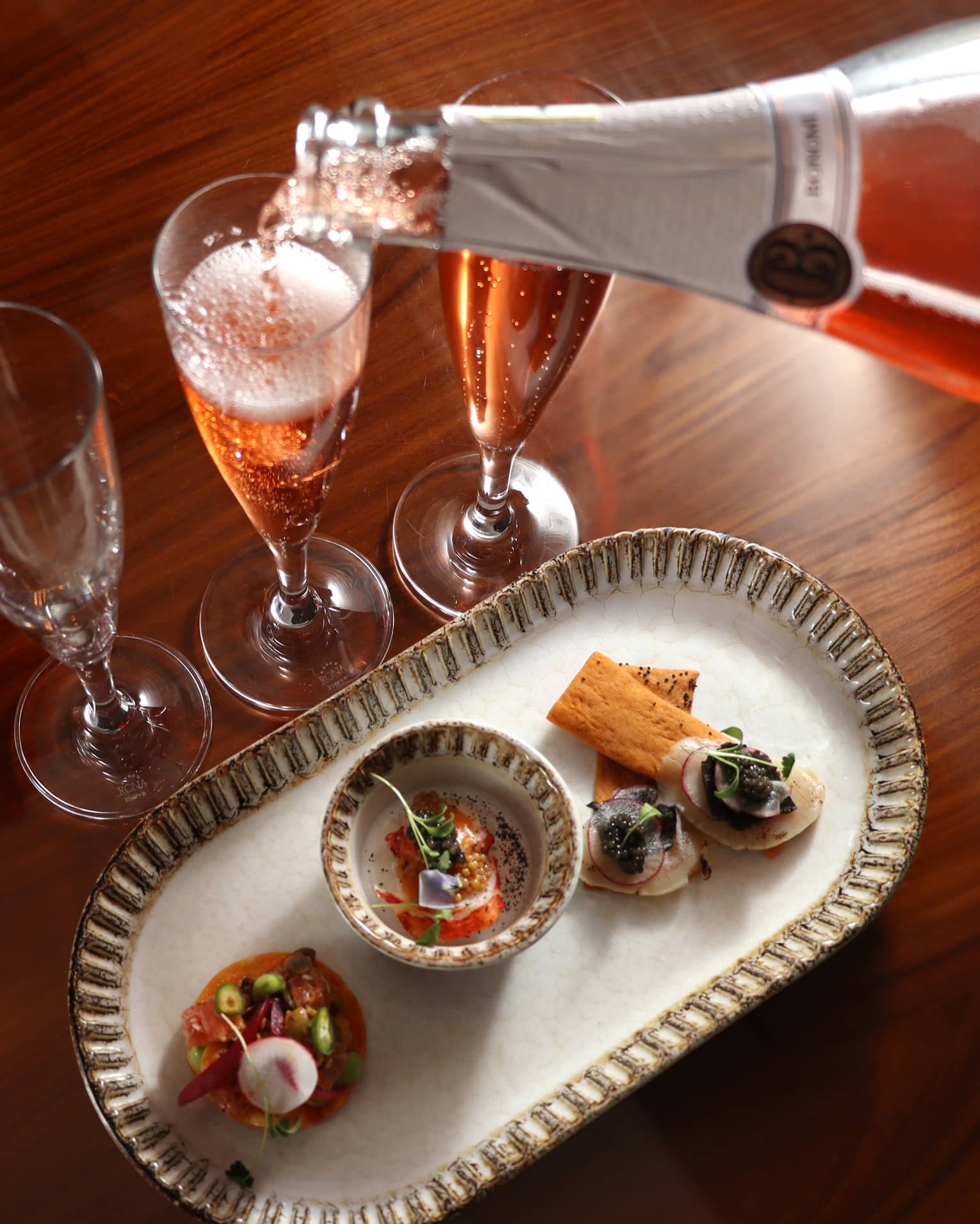 Champagne being poured into a glass beside a food dish