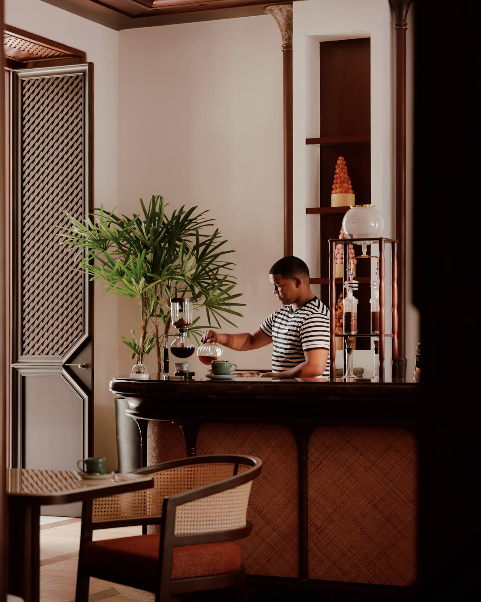 A bartender in a striped t-shirt prepares cocktail behind the bar