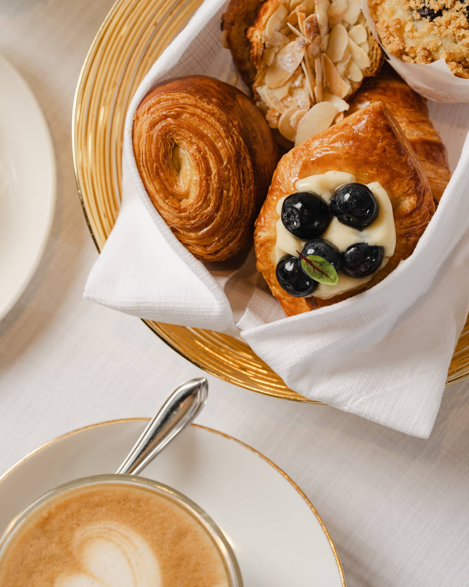 Gold-rimmed bowl filled with breakfast pastries sits on a table next to a white mug of coffee