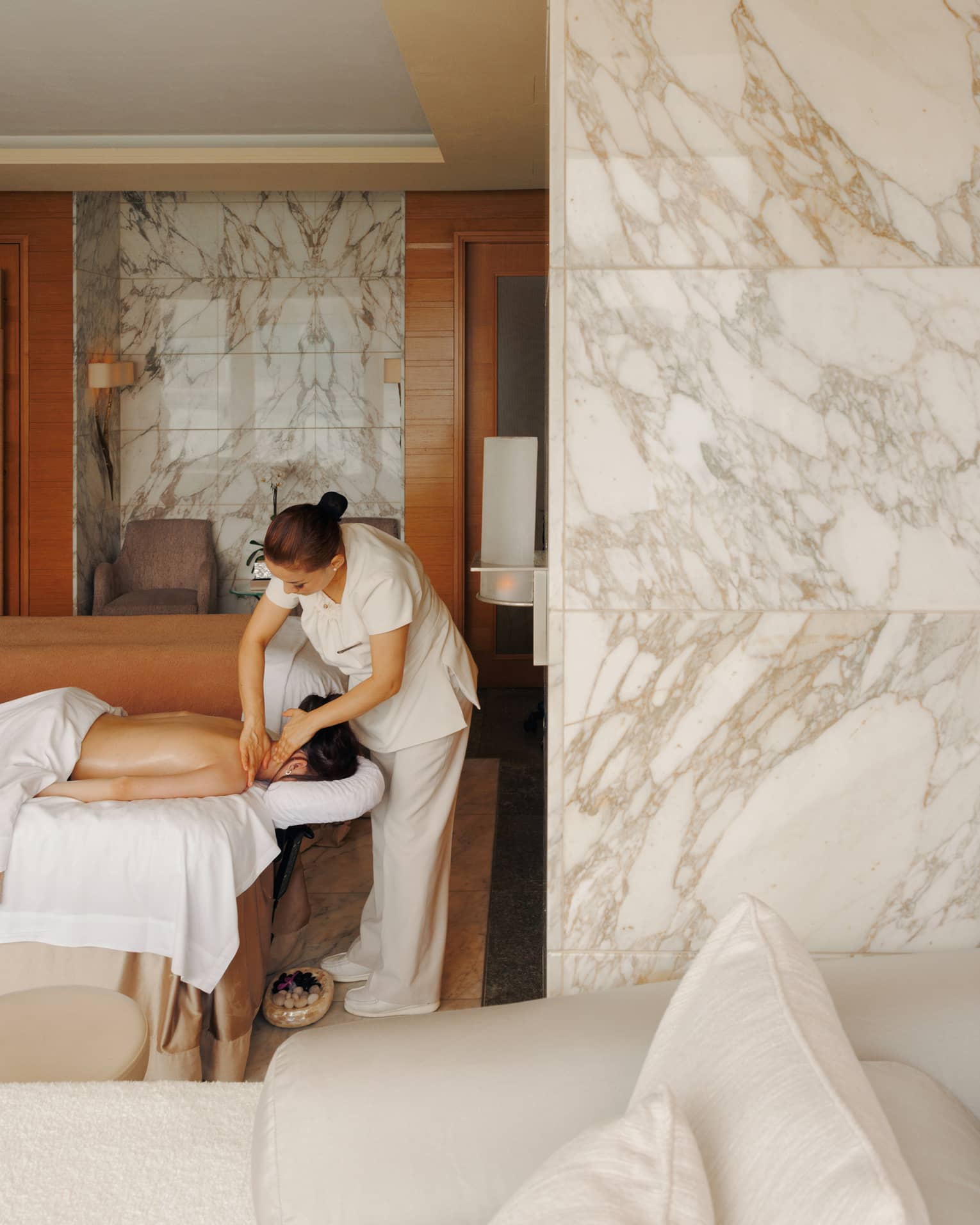 A female spa therapist performing a massage on a woman, face down on spa treatment table, in a chic luxury spa with marble walls