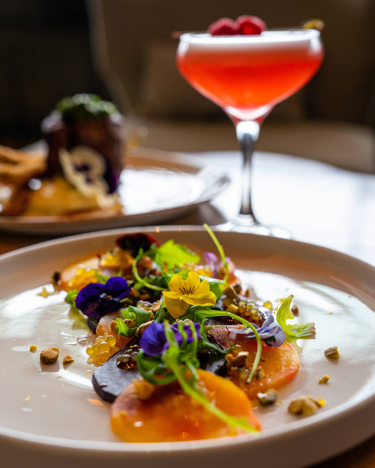 A colourful salad on a white plate with a red cocktail.