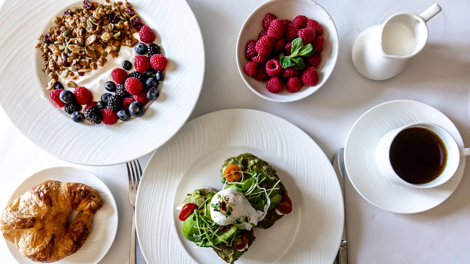 An assortment of food including avocado toast, yogurt, berries, and bread.