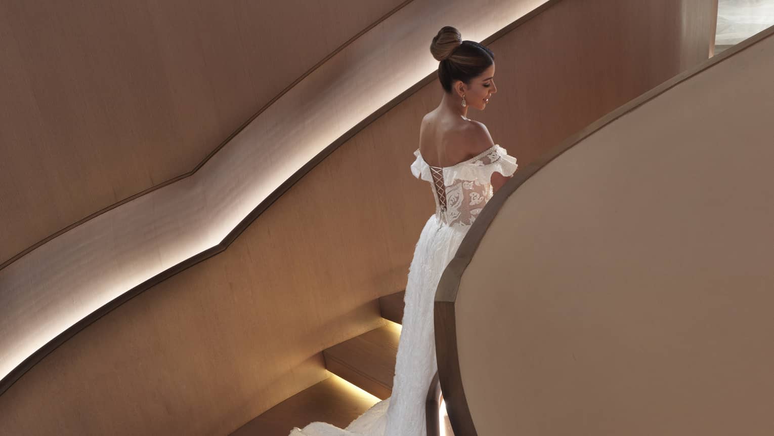Bride with long wedding dress train walks down modern spiral staircase with lights