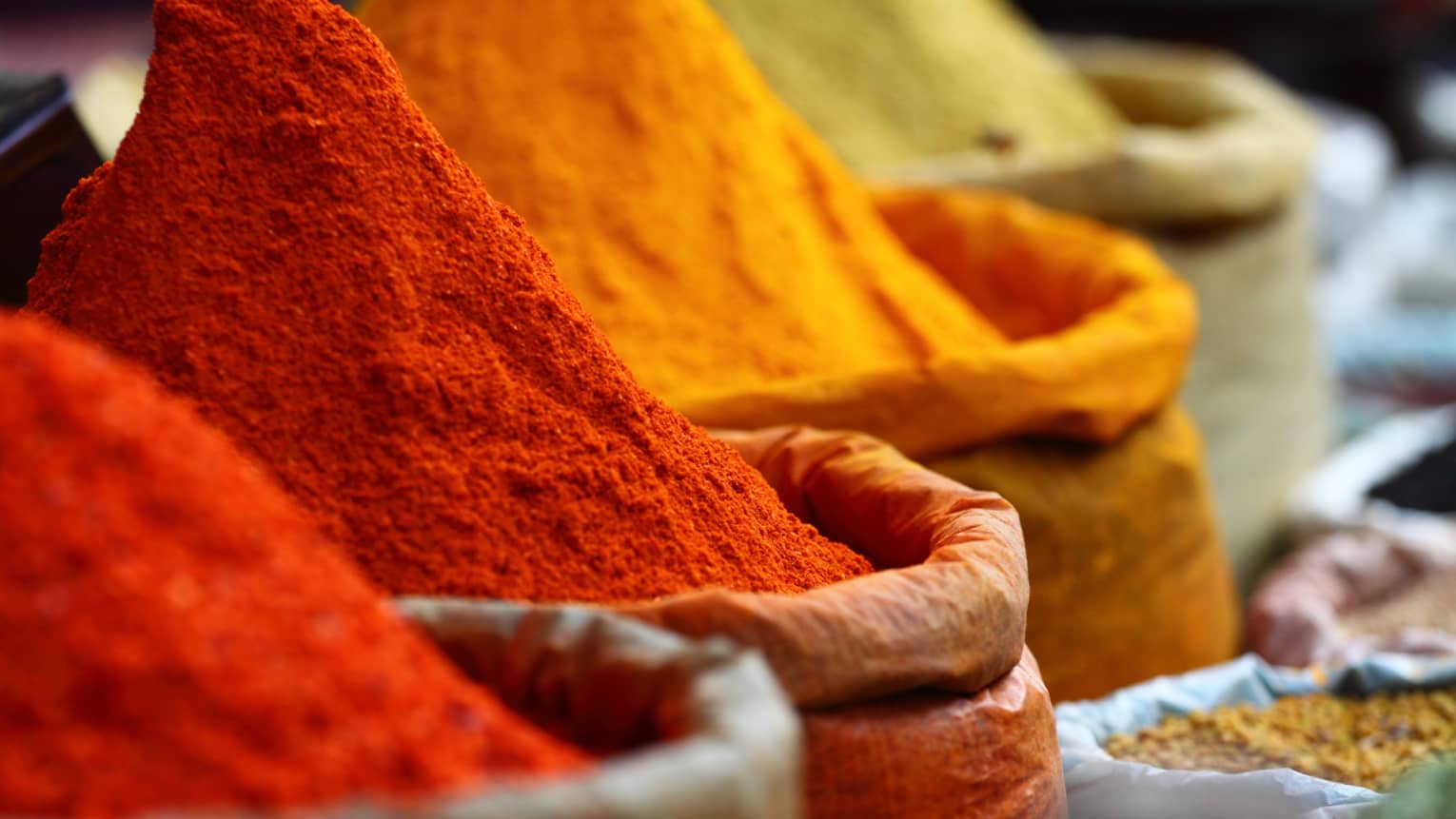 Row of bags overflowing with colourful orange, yellow powdered spices 