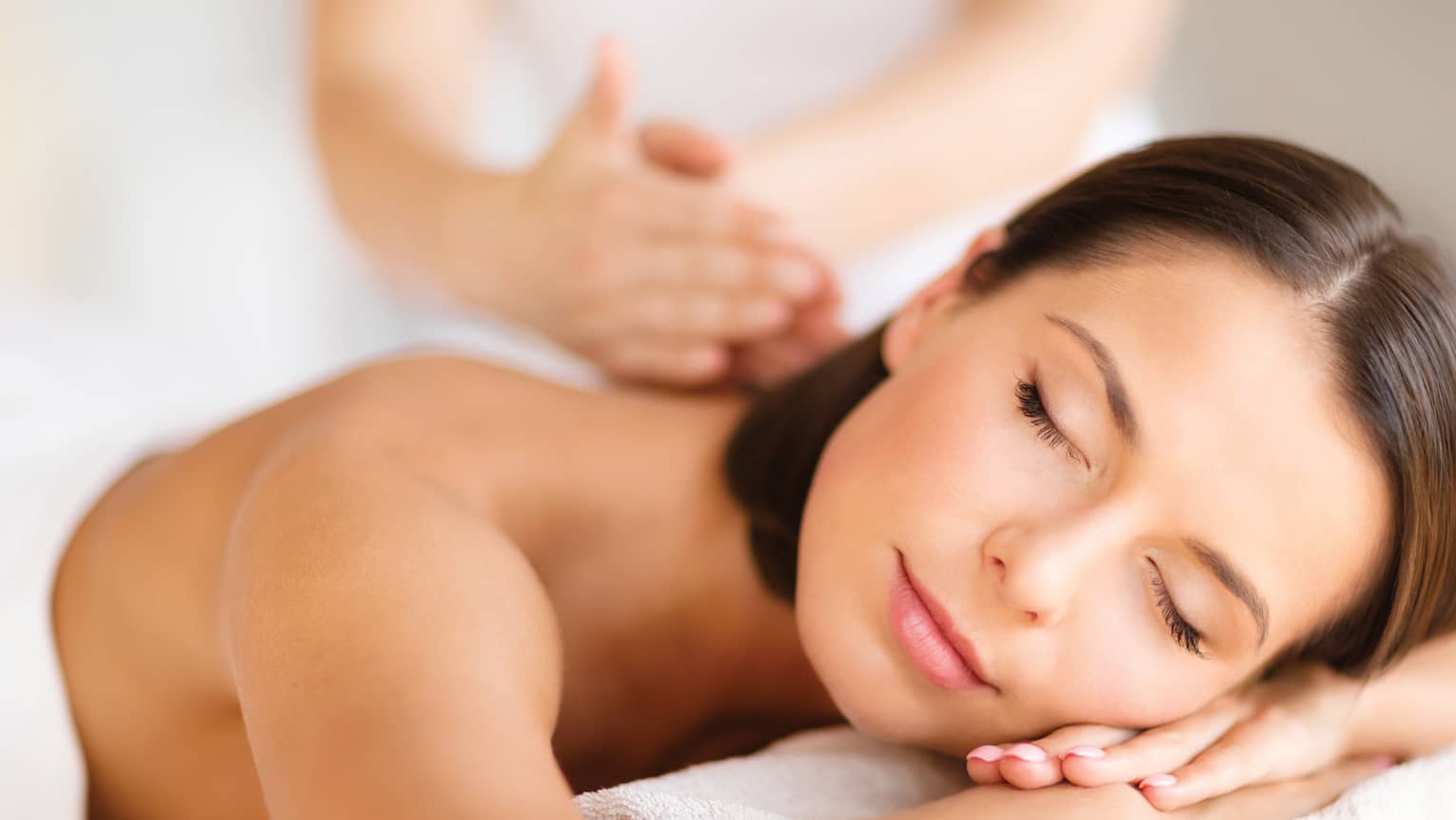 Woman lies on massage table, closes eyes. rests head on arms as spa staff massages back