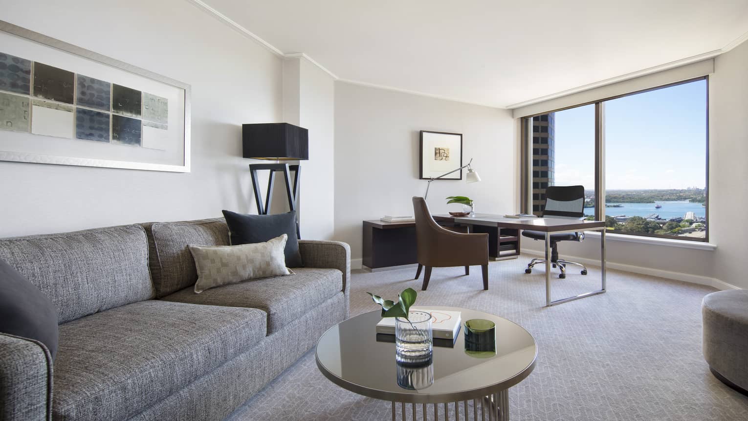 One Bedroom City Suite living area with grey sofa and ottoman, writing desk, round coffee table, views of the Harbour