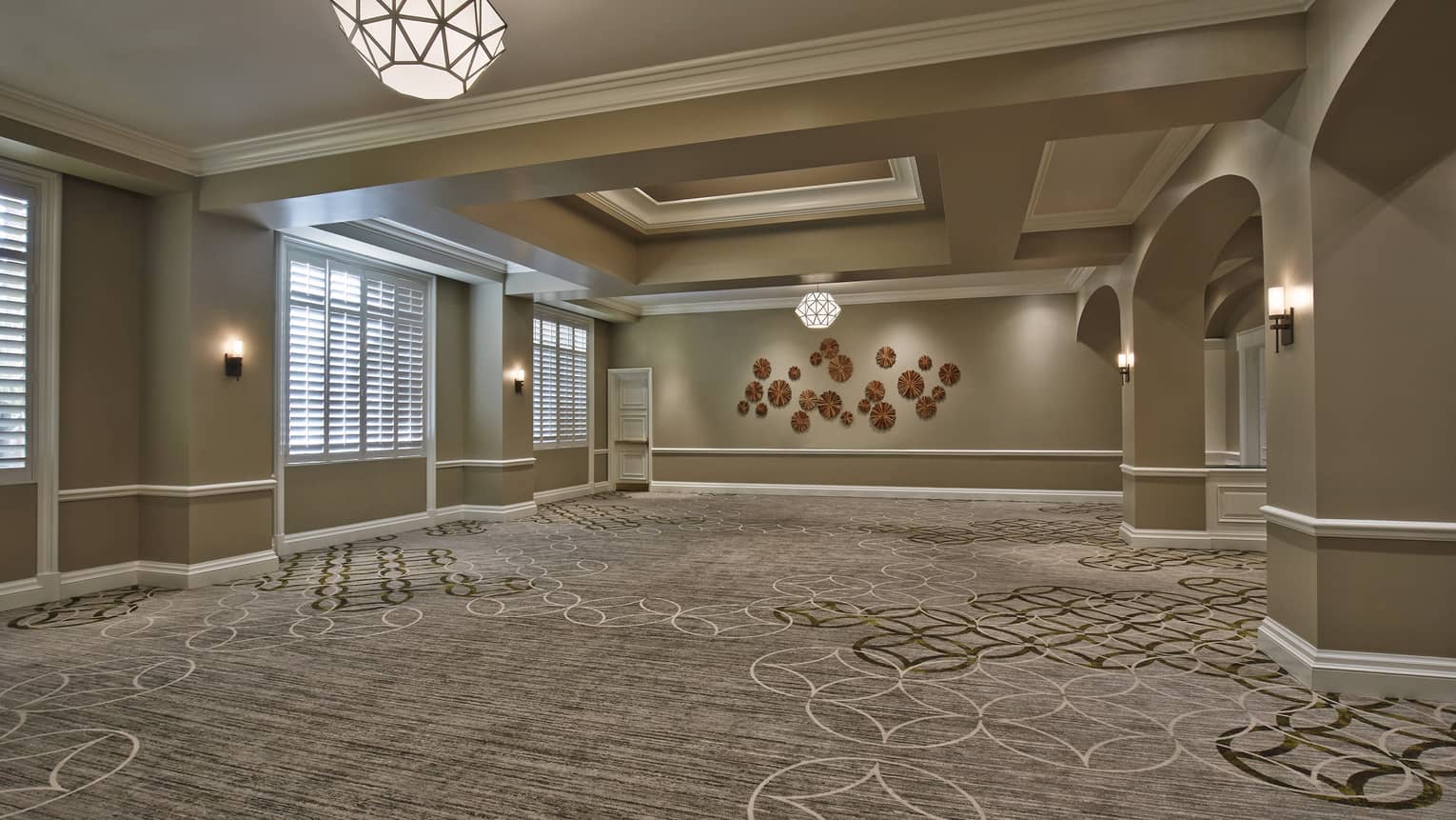 A spacious ballroom with patterned carpet, modern overhead light fixtures and circular wall art