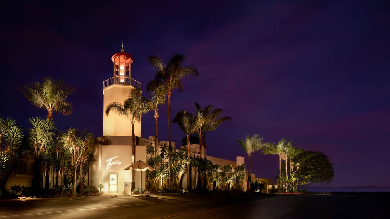 Tydes exterior at night with glowing tower, tall palm trees 
