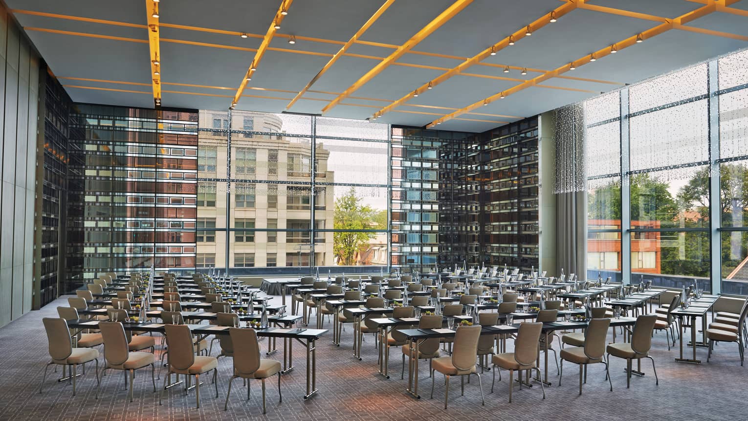 Chairs, tables set up in rows in glass room with corner windows 