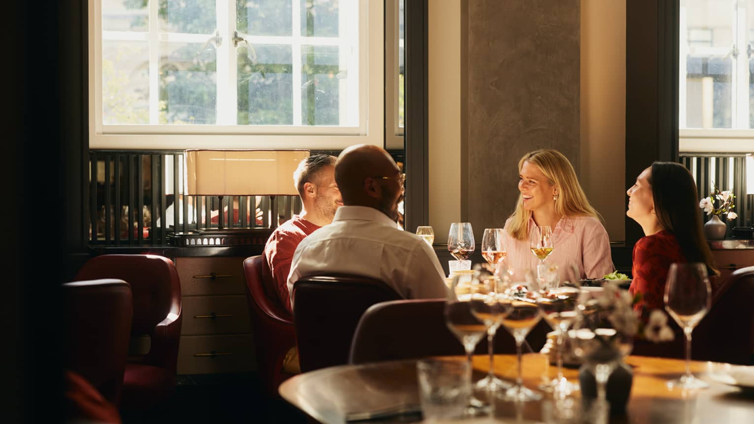 People sitting around a table, enjoying a meal in an indoor dining space. The table is next to a window that is letting in bright natural light.