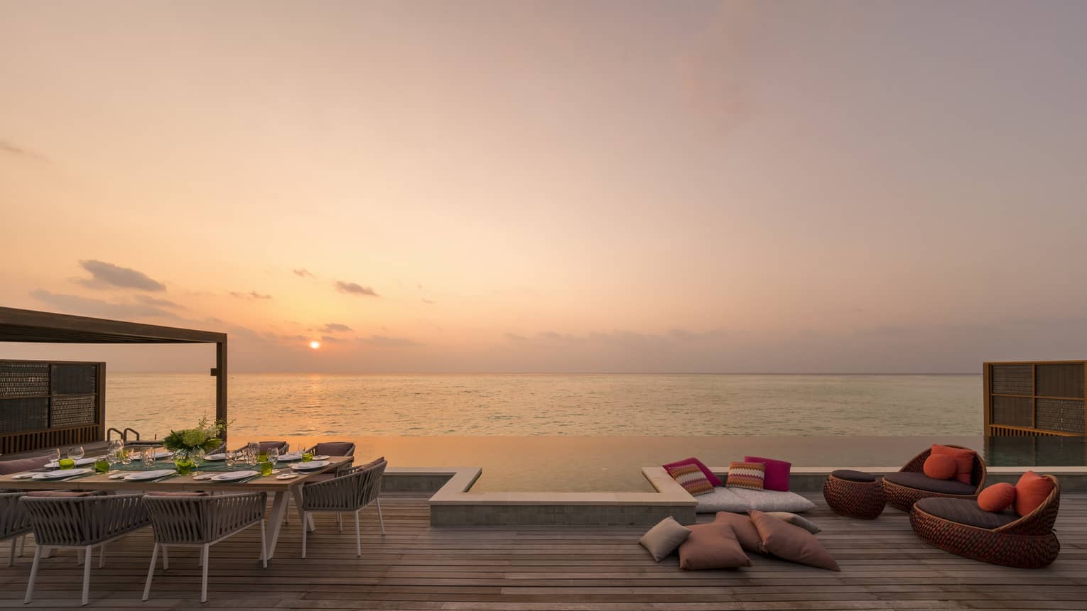 Outdoor deck with a dining table, lounge seating and an infinity pool overlooking the ocean at sunset