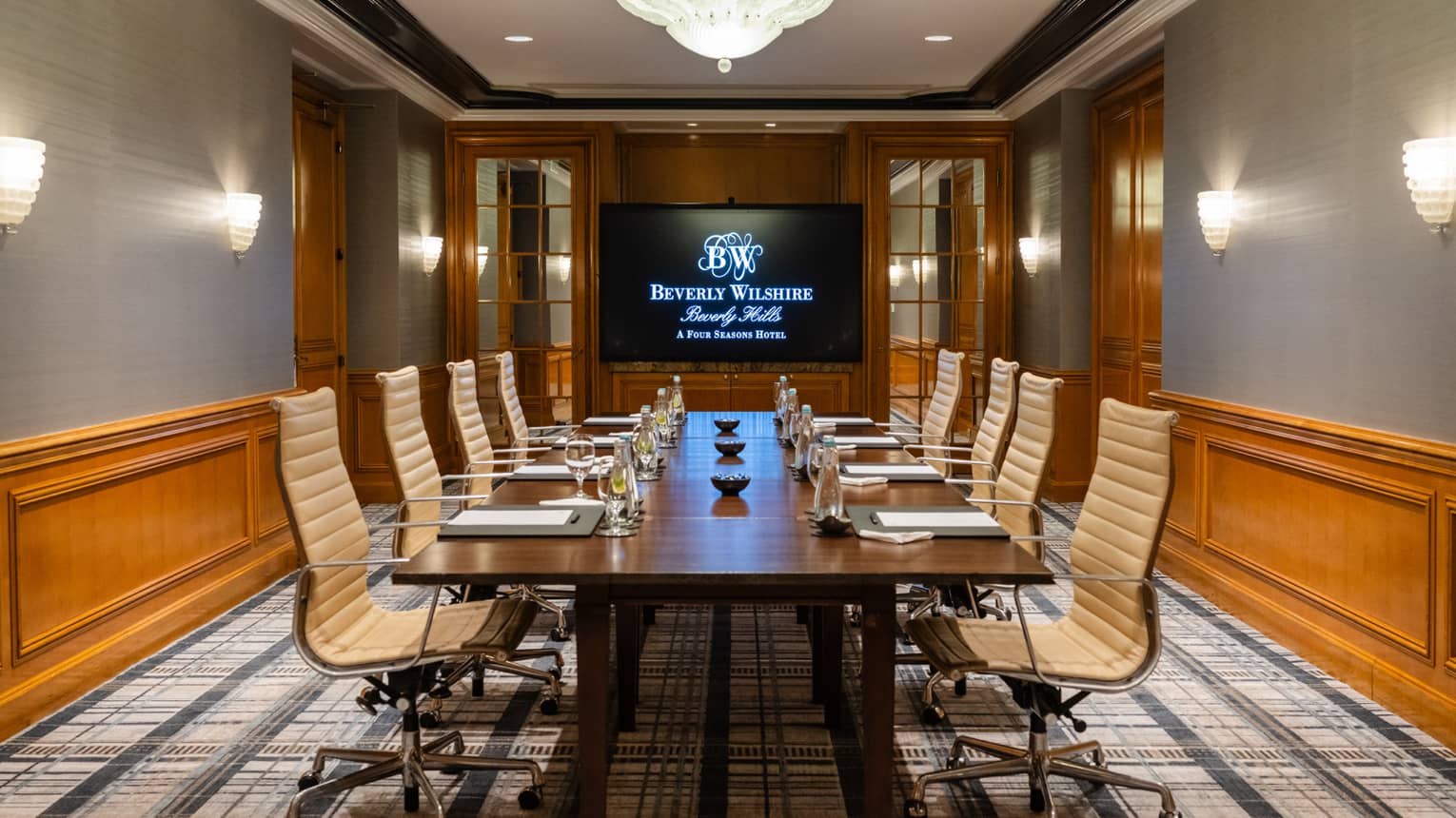 A meeting room with lights on the walls and a monitor, and a table with papers at each seat
