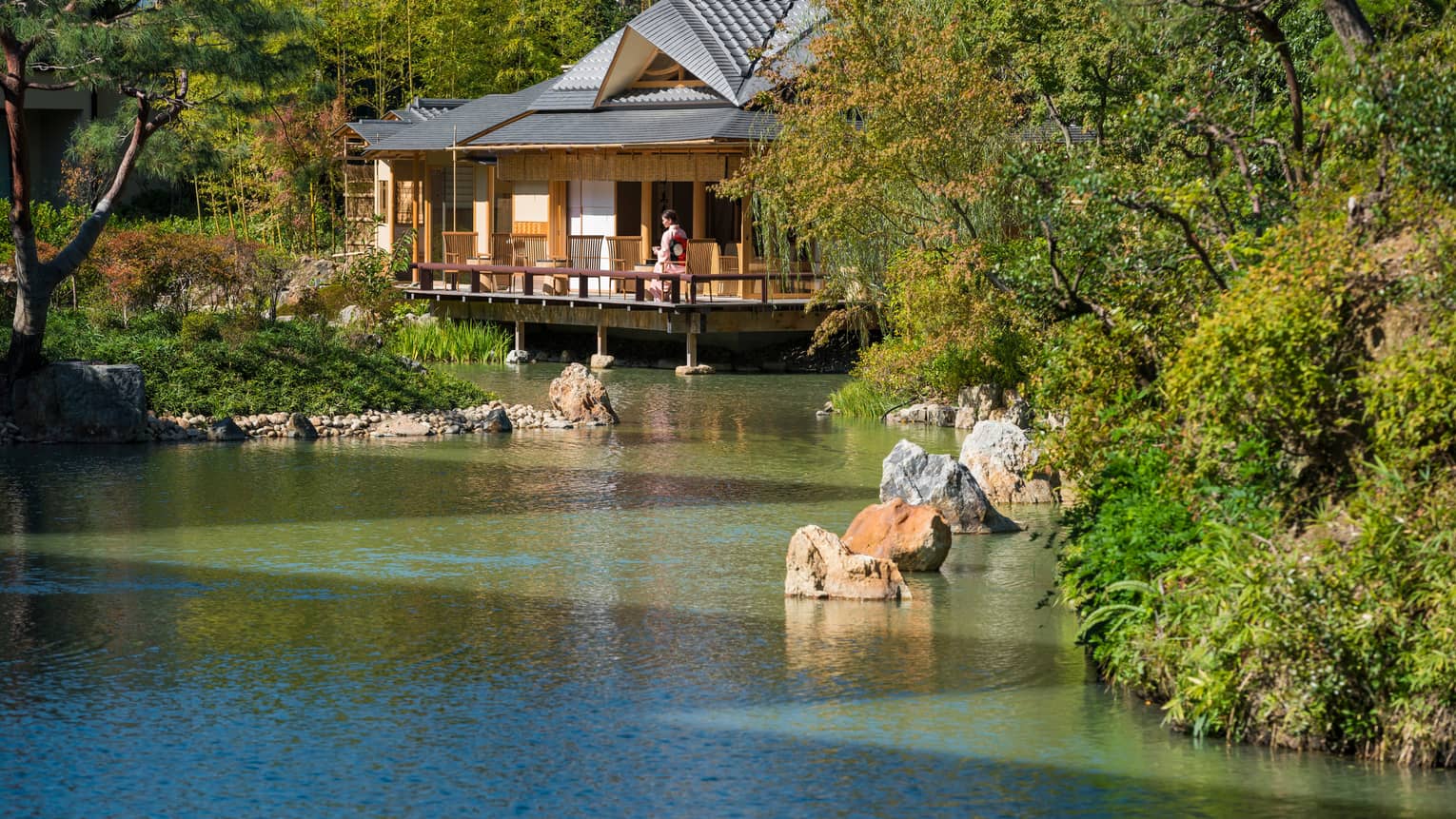 View across pond to bungalow where woman in robe sits on patio