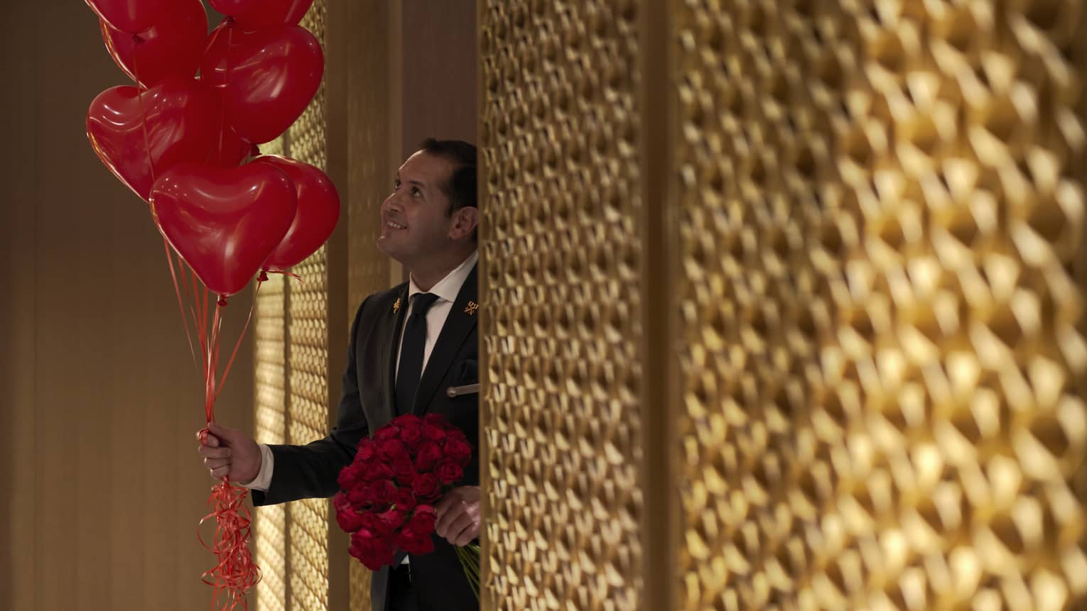Male hotel staff member carries bunch of read heart balloons